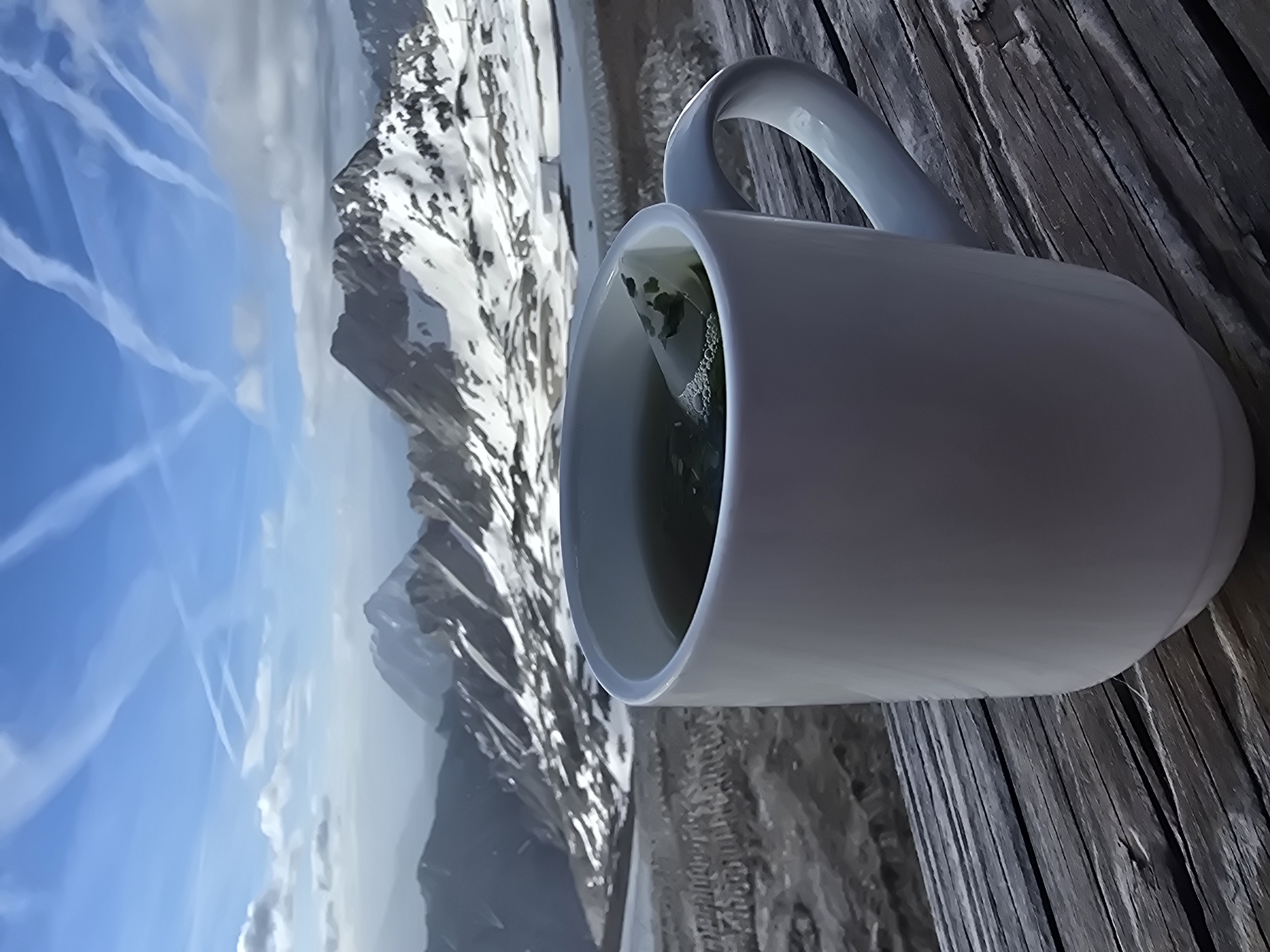 Hot drink on a wooden railing, Alpine peaks behind