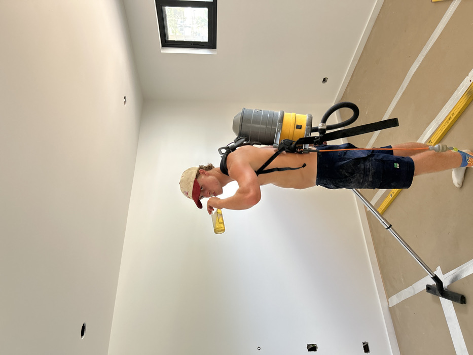 Construction worker vacuums unfinished room while drinking beer in Stanwell Tops