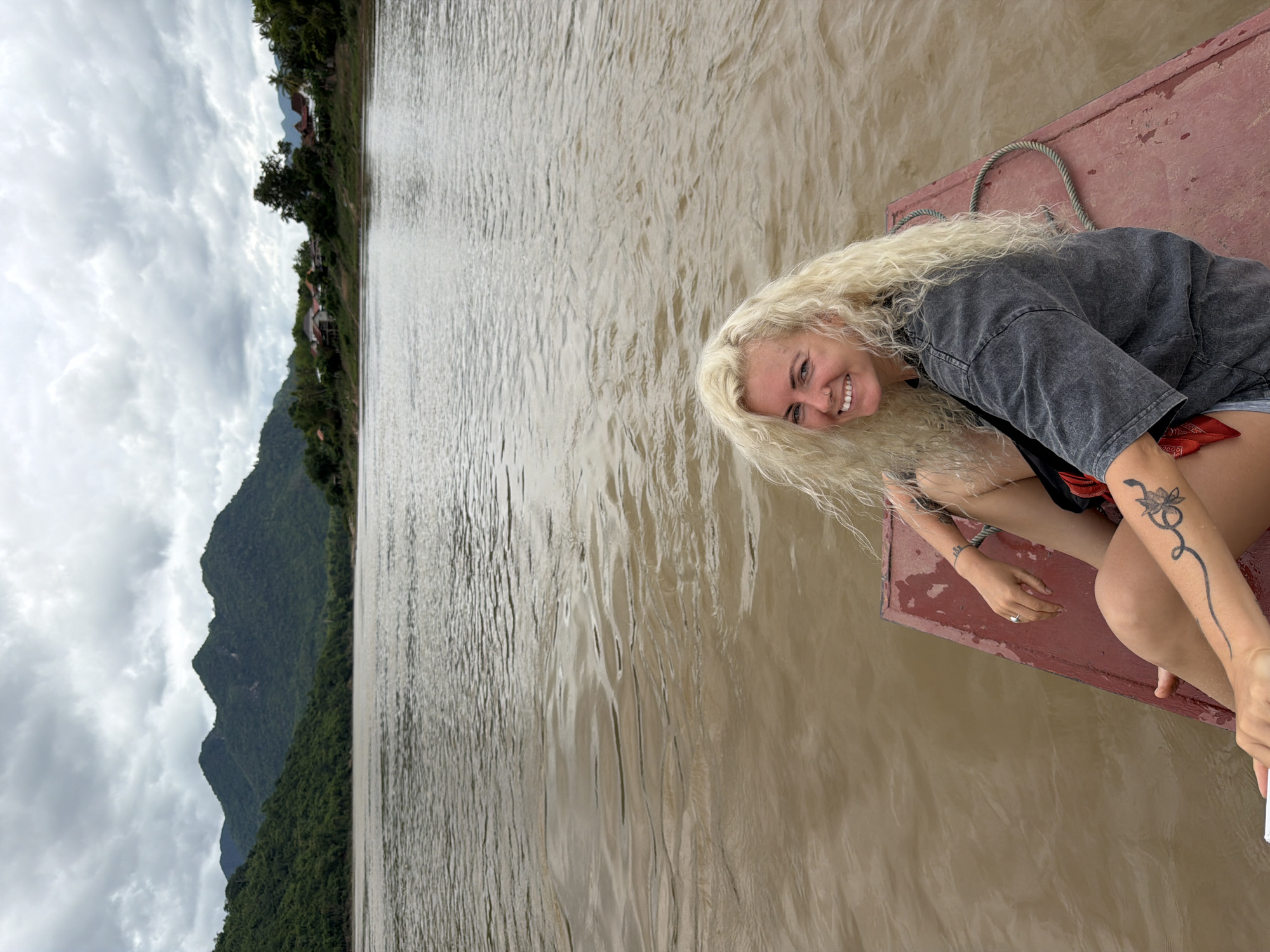 Drifting down a muddy Laotian river on a red wooden boat