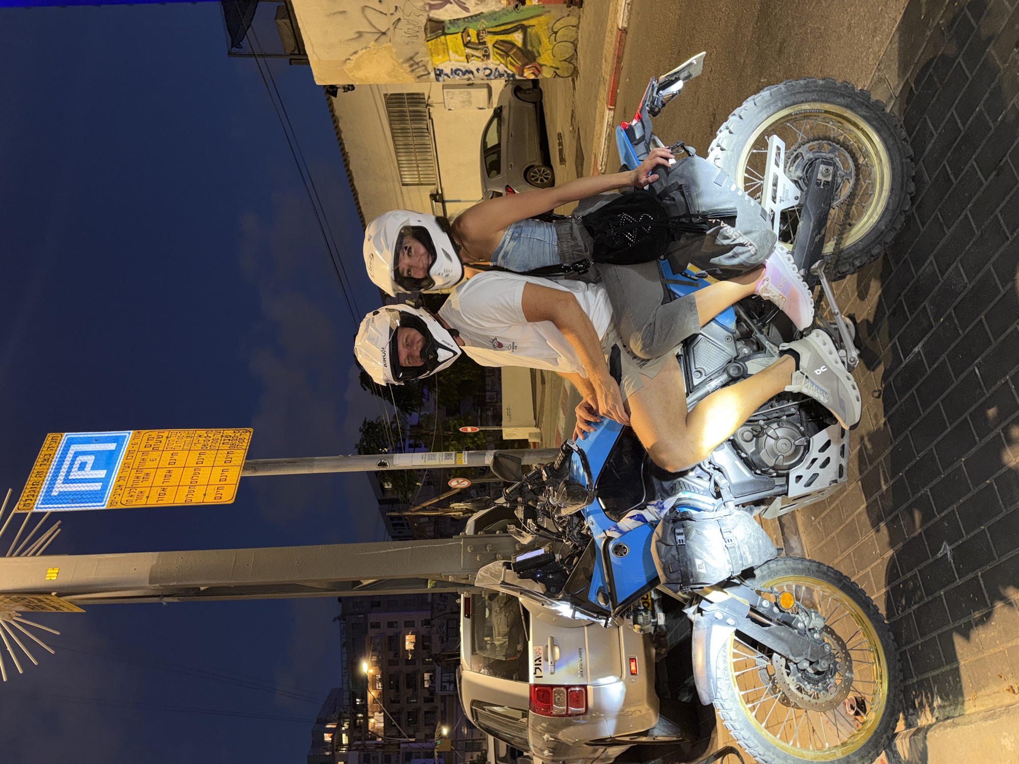Helmeted duo on a blue motorcycle, Tel Aviv night