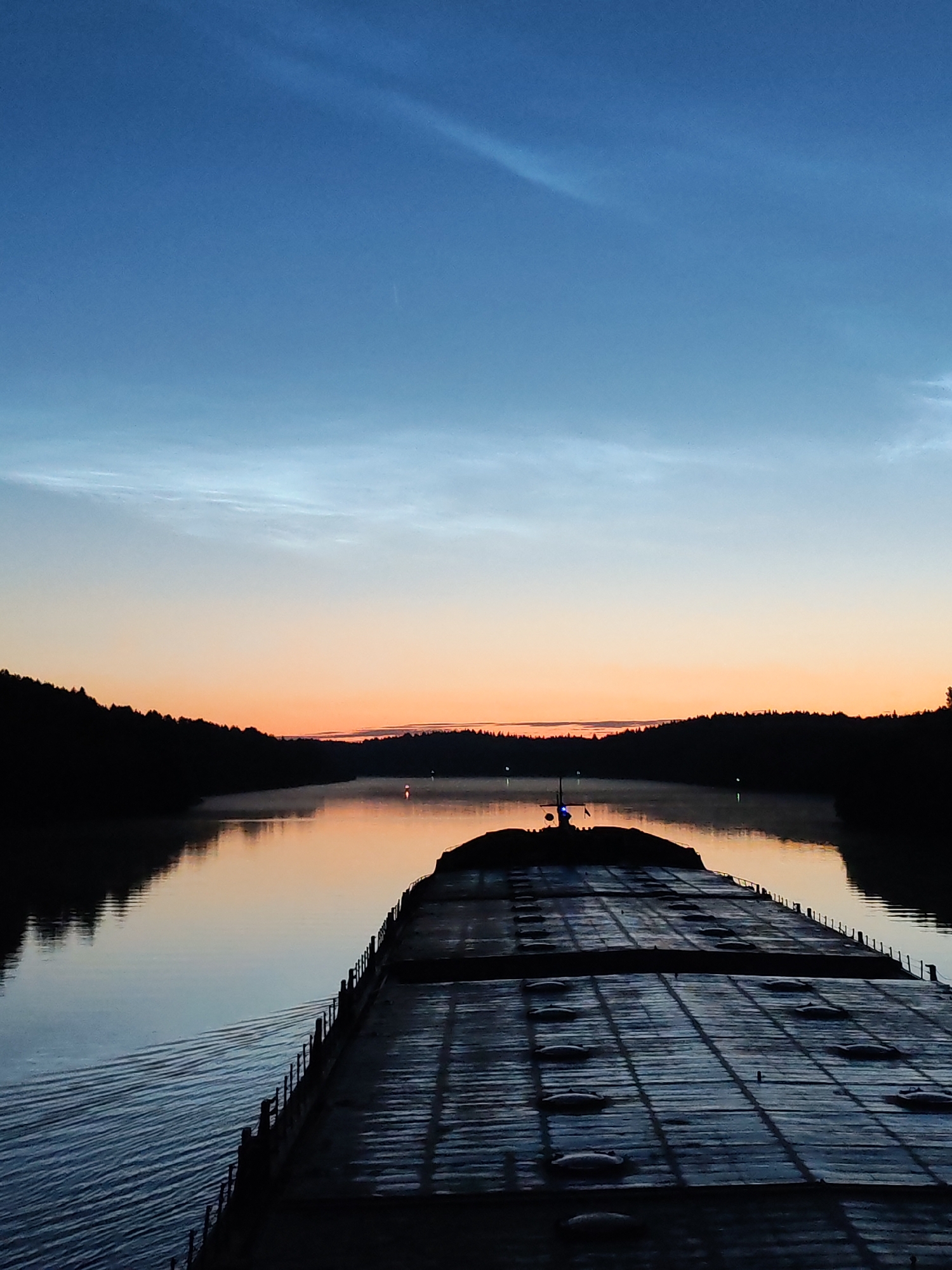 Drifting past forested riverbanks under a noctilucent sky
