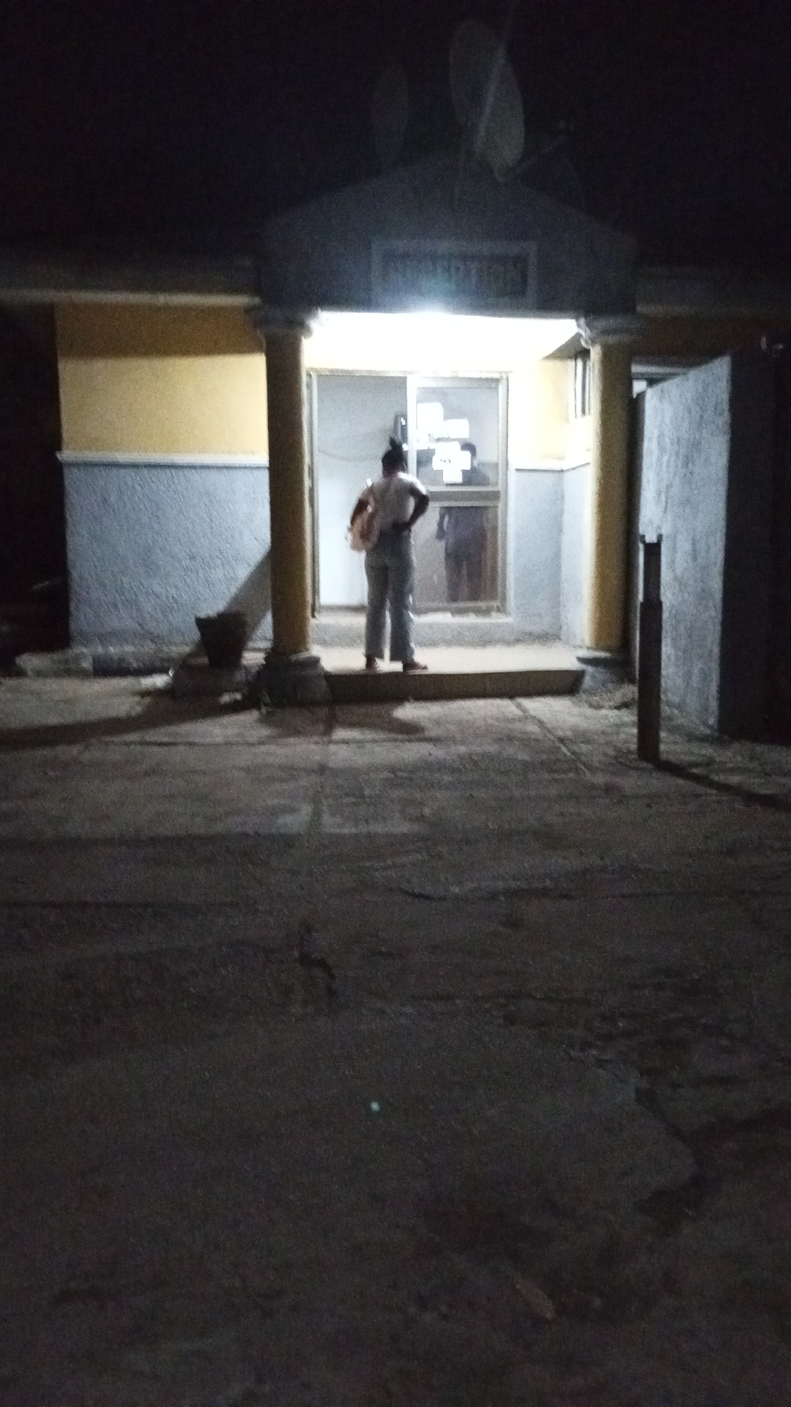 Person stands at illuminated building entrance in Adankolo