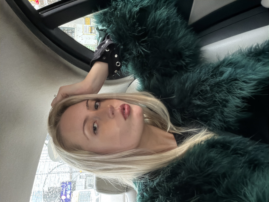 Woman in feathered coat poses for photo in London car