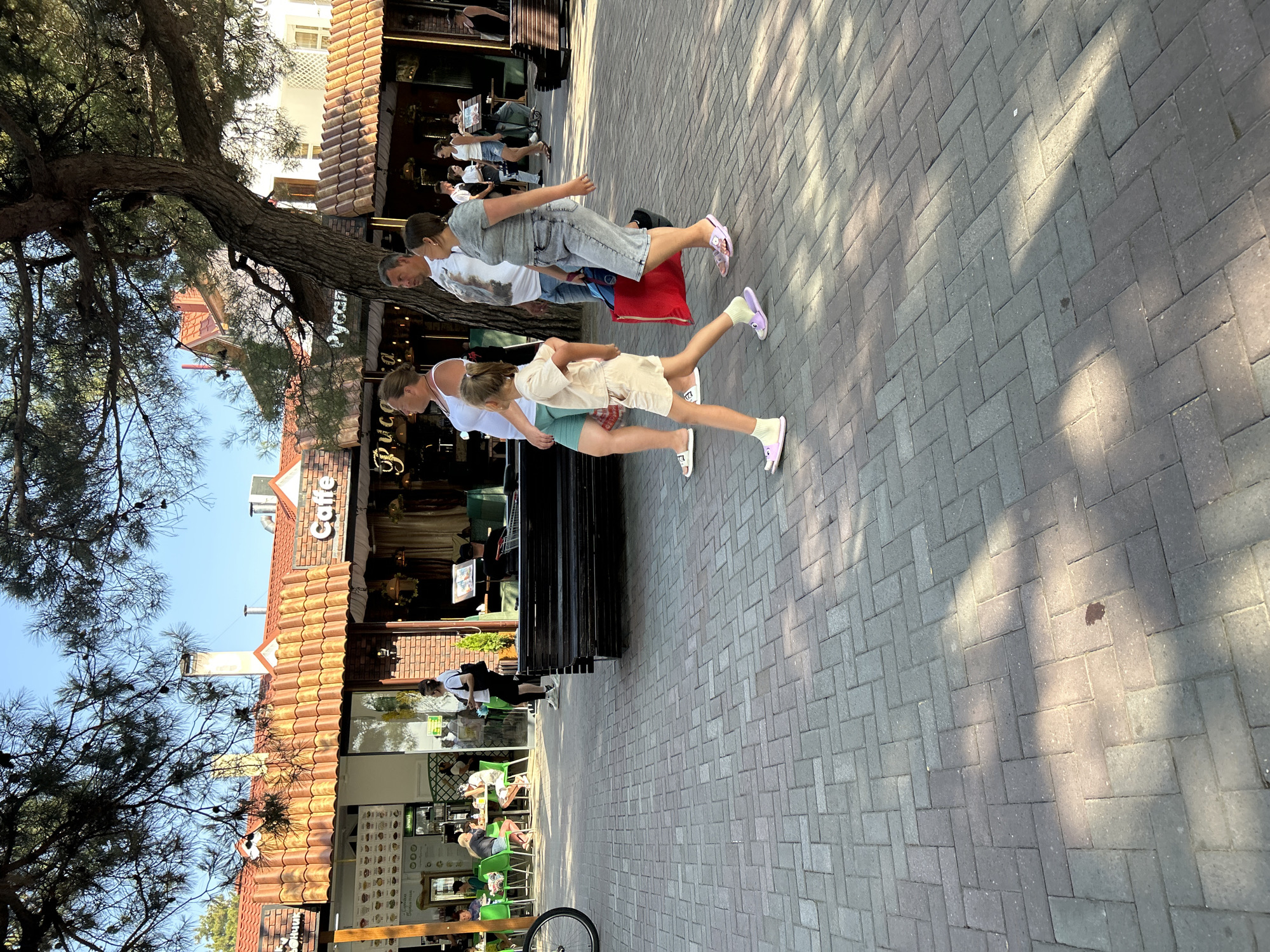 Street performer, pedestrians, and scooters fill a sunny urban stretch