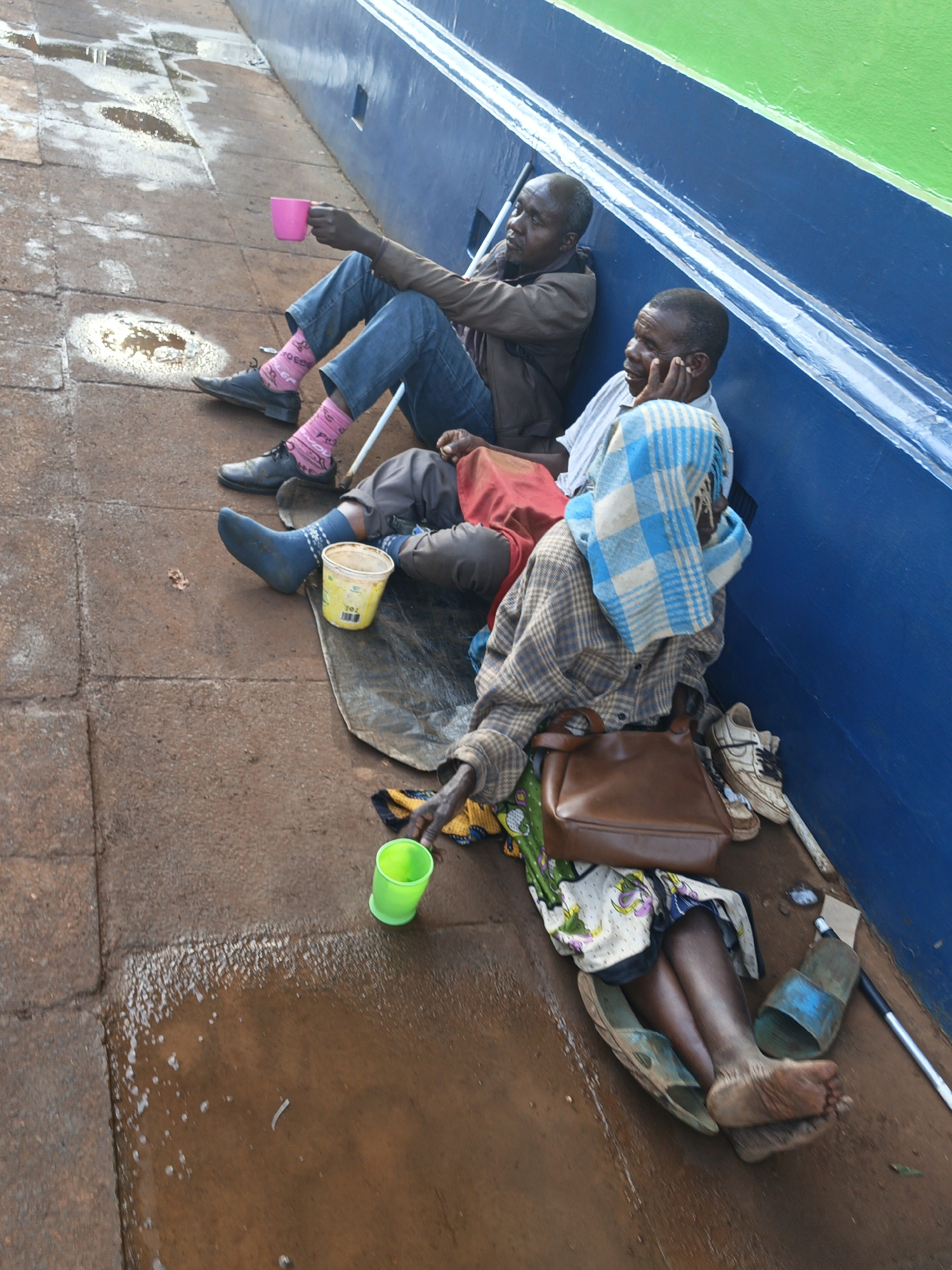Three people sit against blue wall in Thika, Kenya