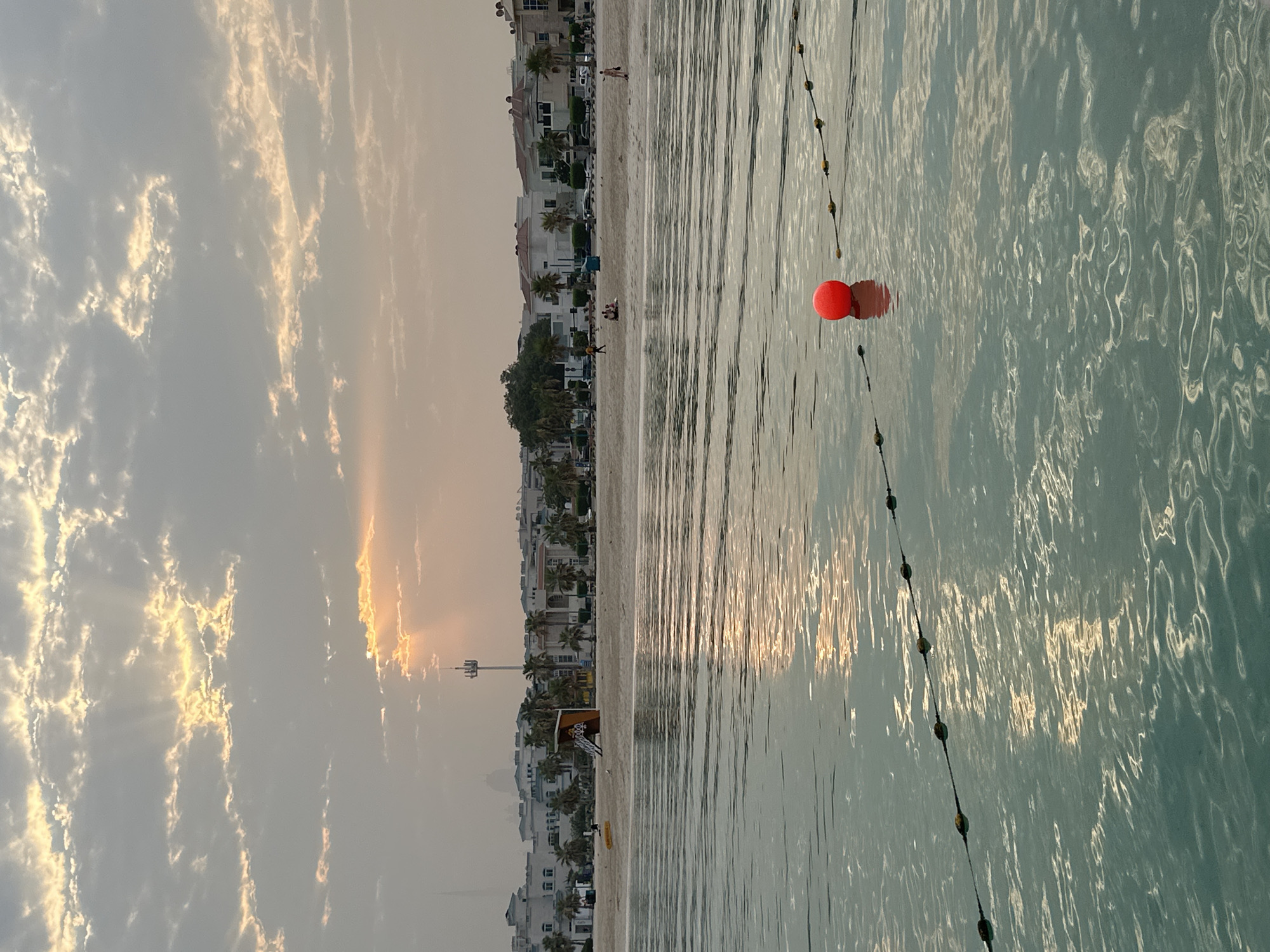 Dubai beachfront at golden hour, calm water and cloudy skies