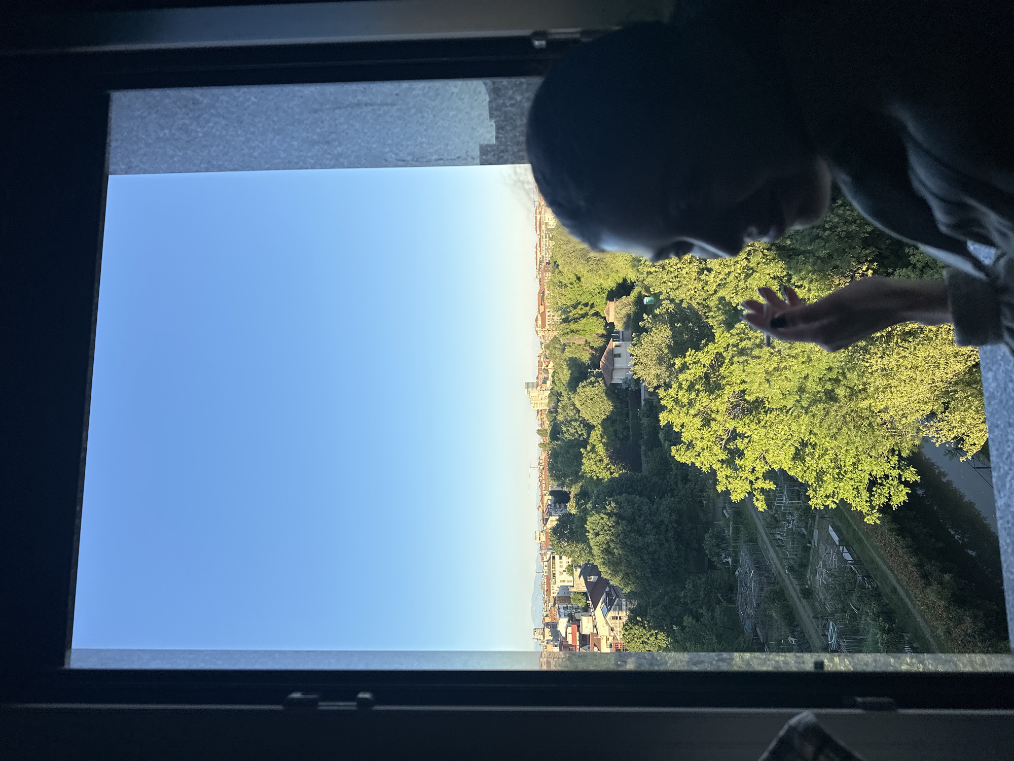 Person observes Milan cityscape from window on clear afternoon
