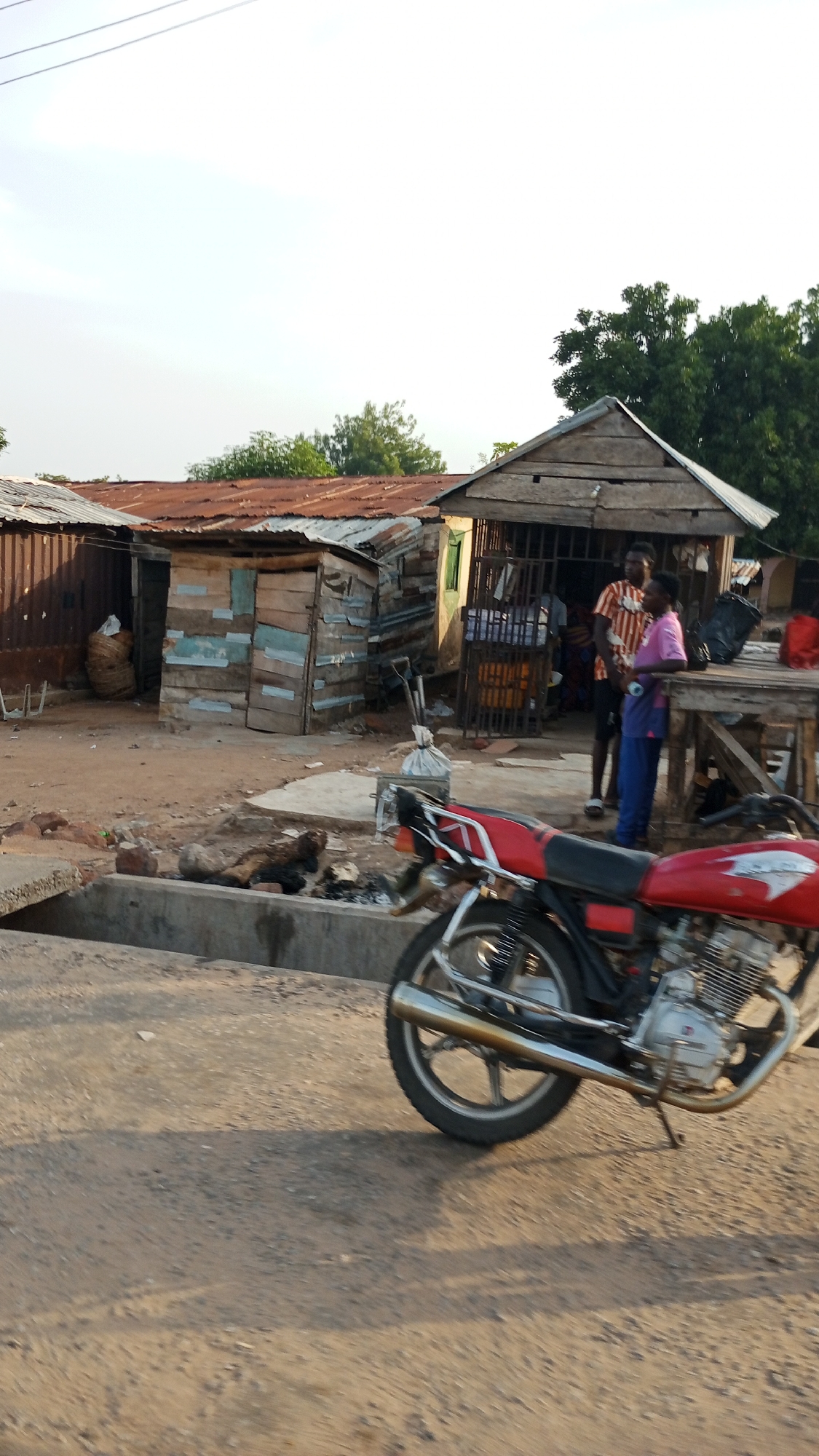 Morning scene captured in Zango-ndaji: motorcycle, pedestrian, dirt road