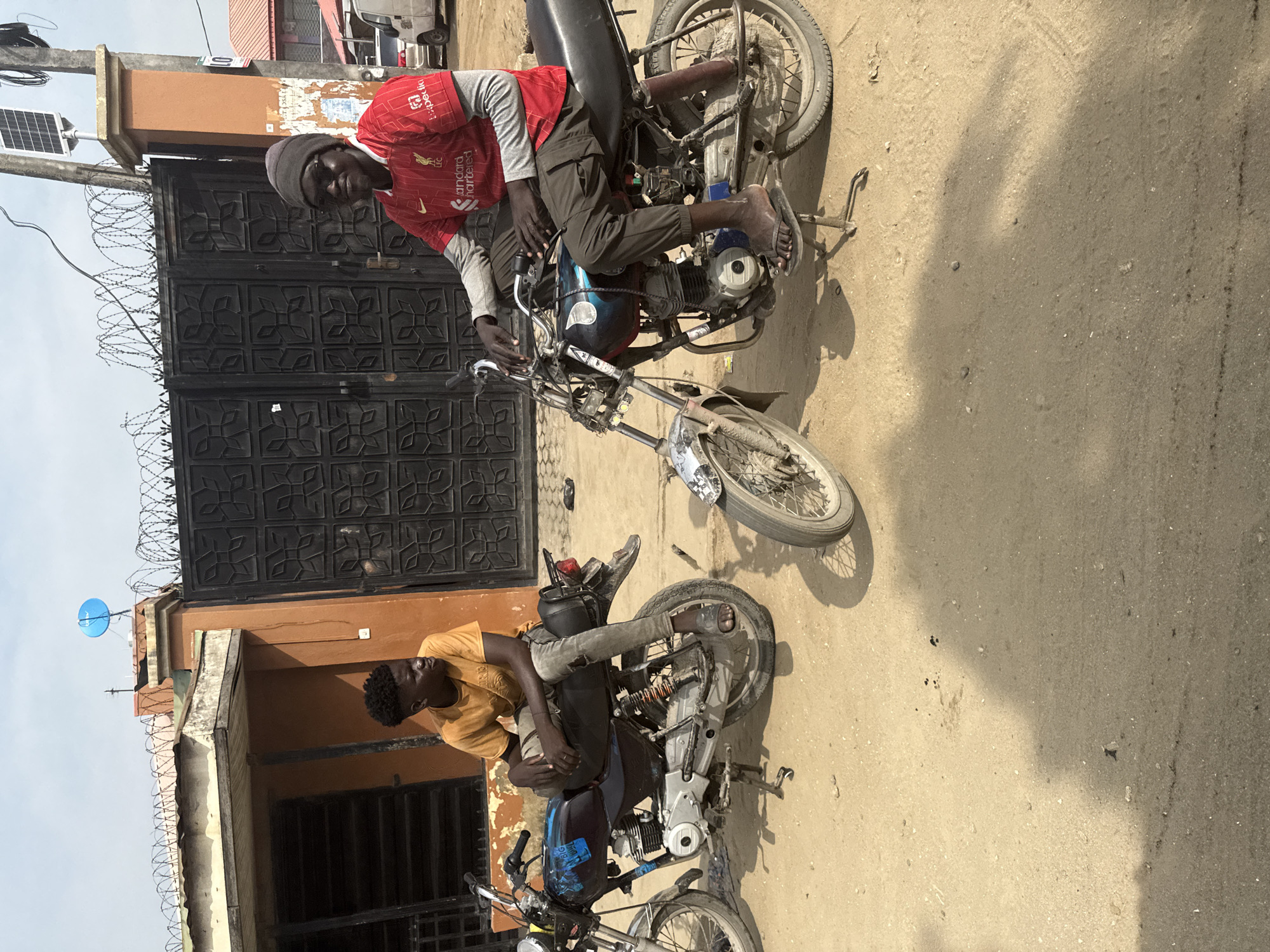 Two men with motorcycles spotted on dusty road in Ado, Nigeria