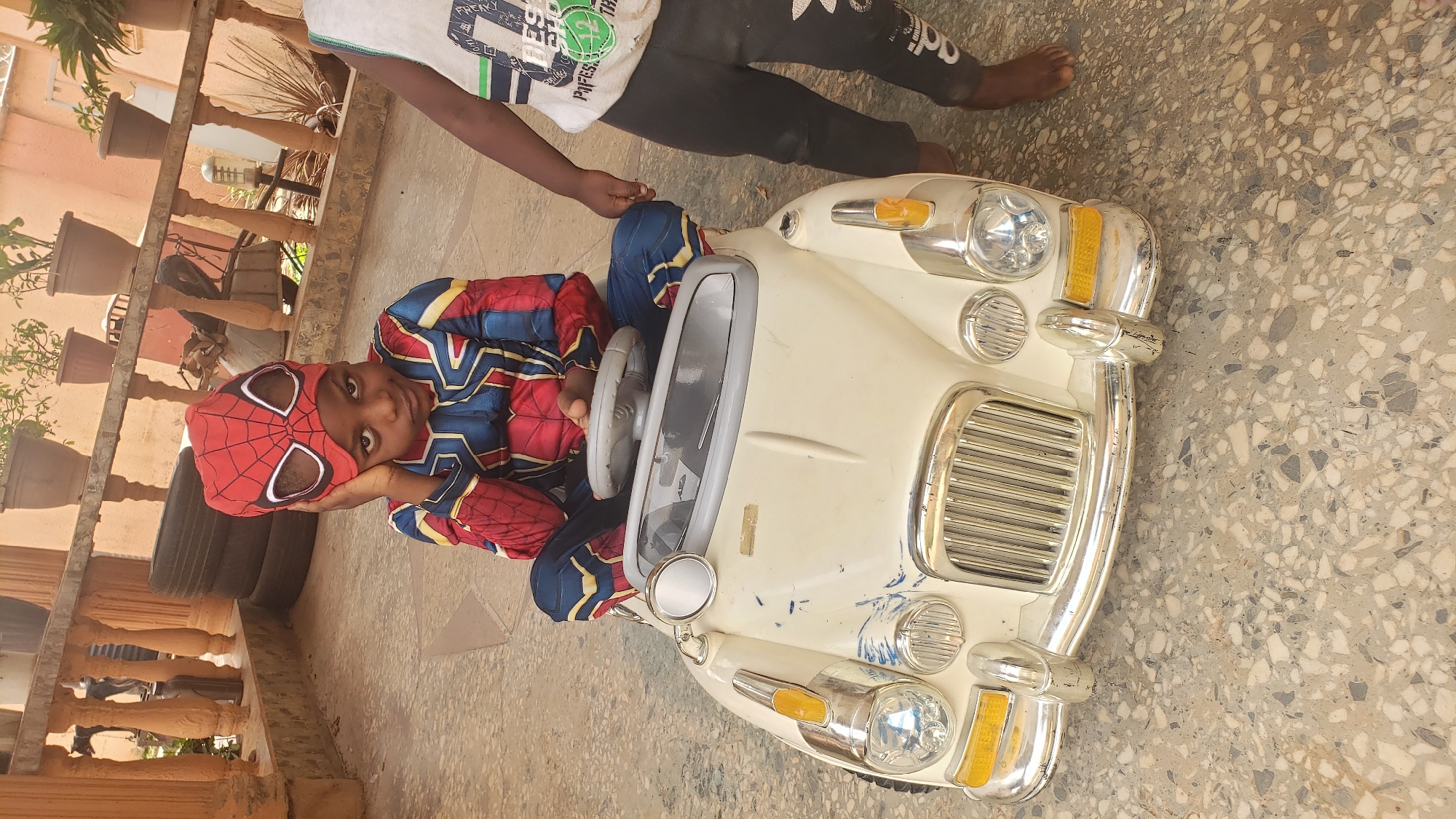 Child in Spiderman costume poses in toy car