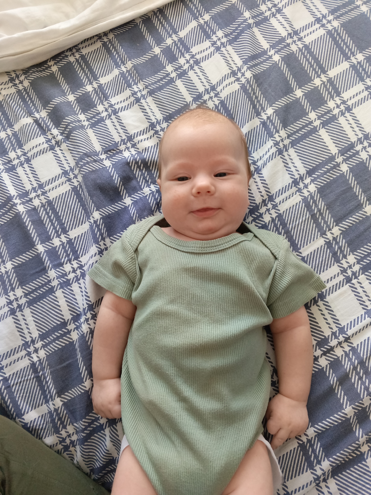 Baby in green onesie plays with mobile in Andreyevo crib