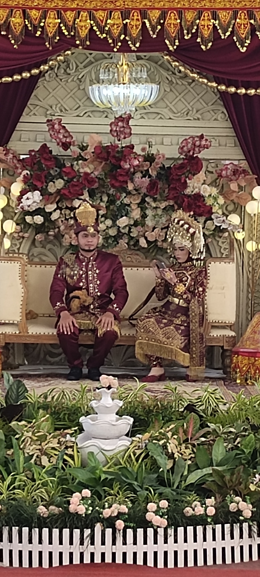 Wedding ceremony documented in traditional burgundy attire at indoor venue