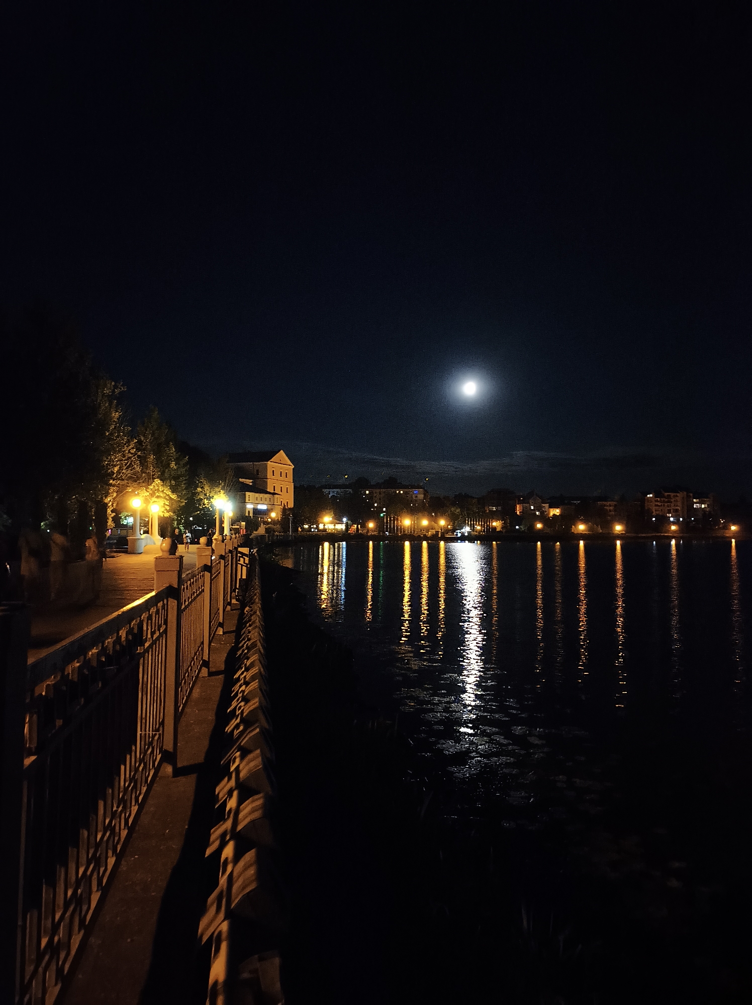 Ternopil lake promenade at night, moon reflected on calm water