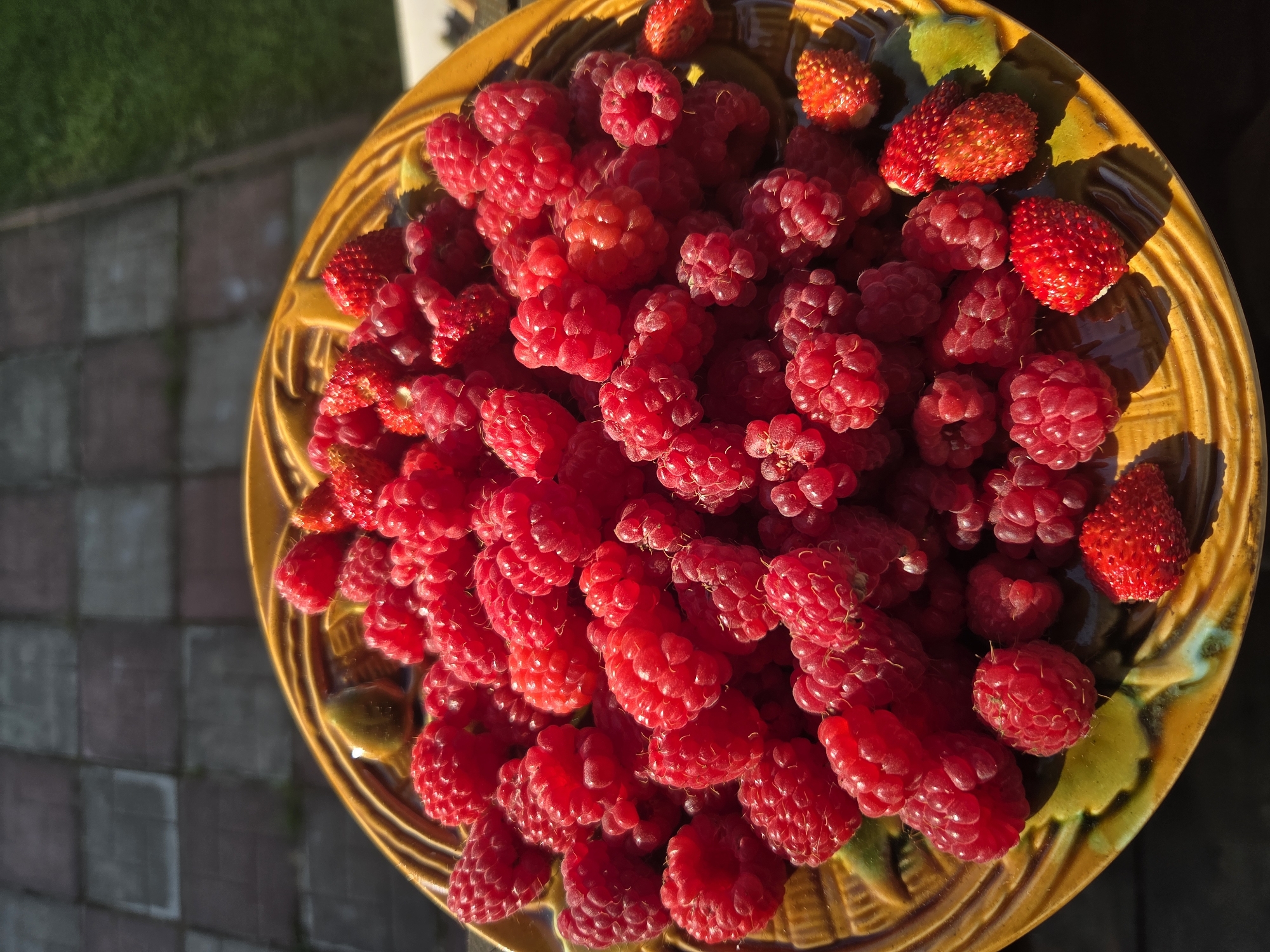 Fresh raspberries and wild strawberries on a yellow ceramic plate