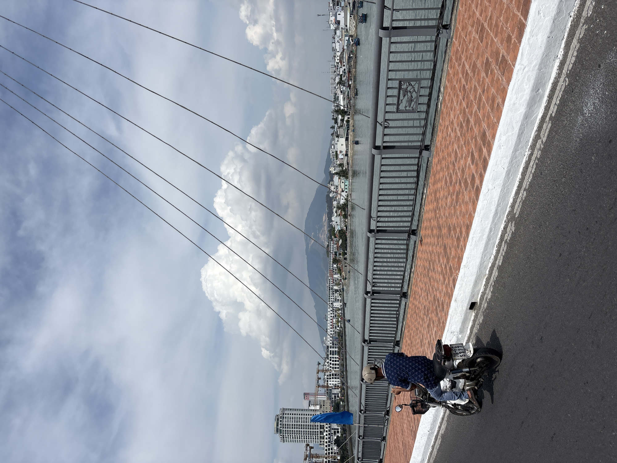 Motorcyclist crosses bridge in Nha Trang under cloudy skies