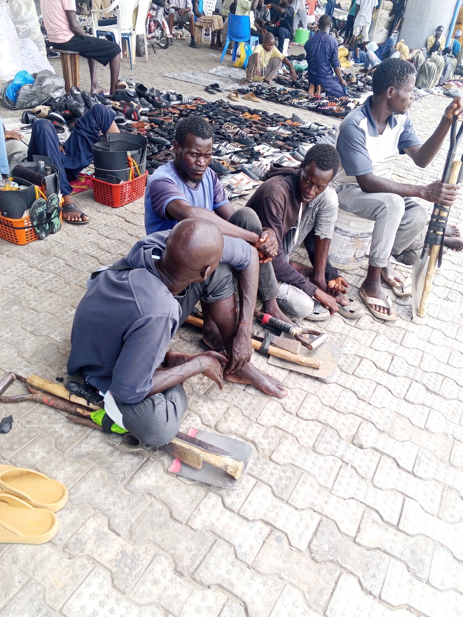 Men gather at outdoor shoe repair market during midday