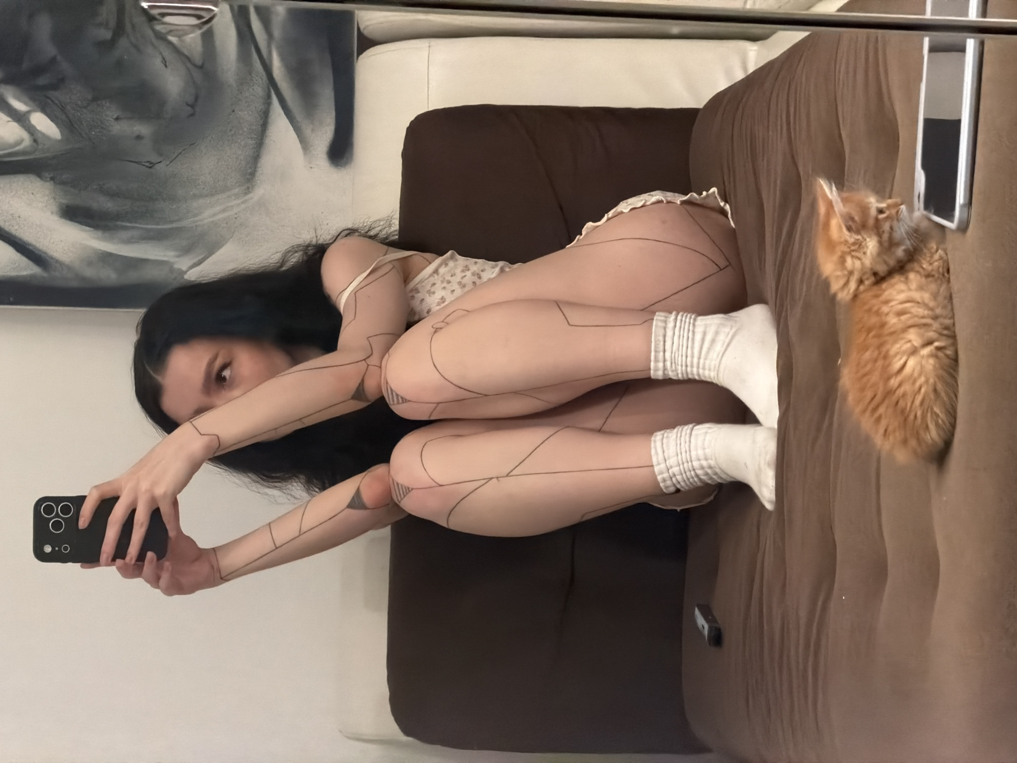 Woman takes selfies with orange cat on sofa