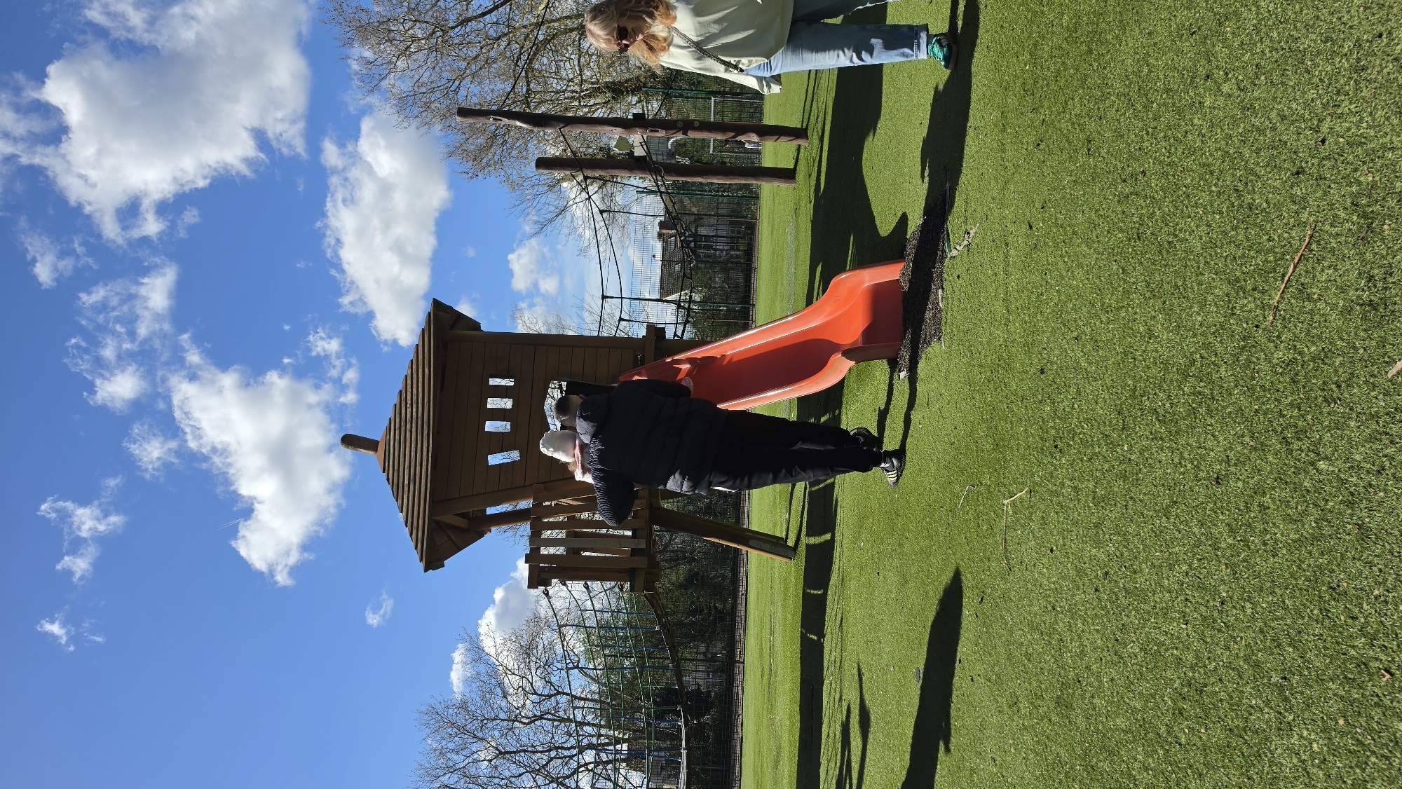 Toddler plays on London playground slide with adult assistance