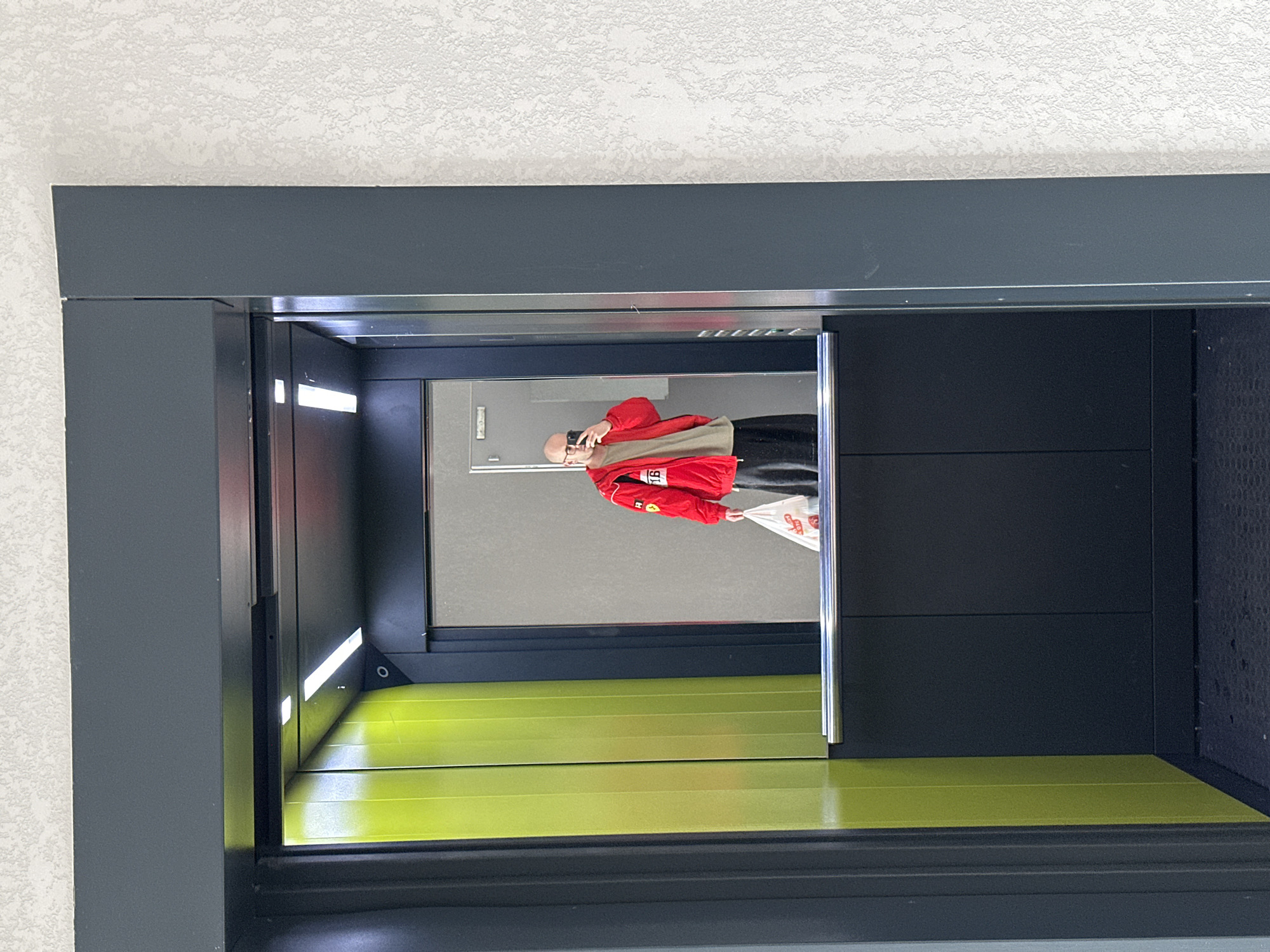 Person in red jacket photographed in elevator mirror