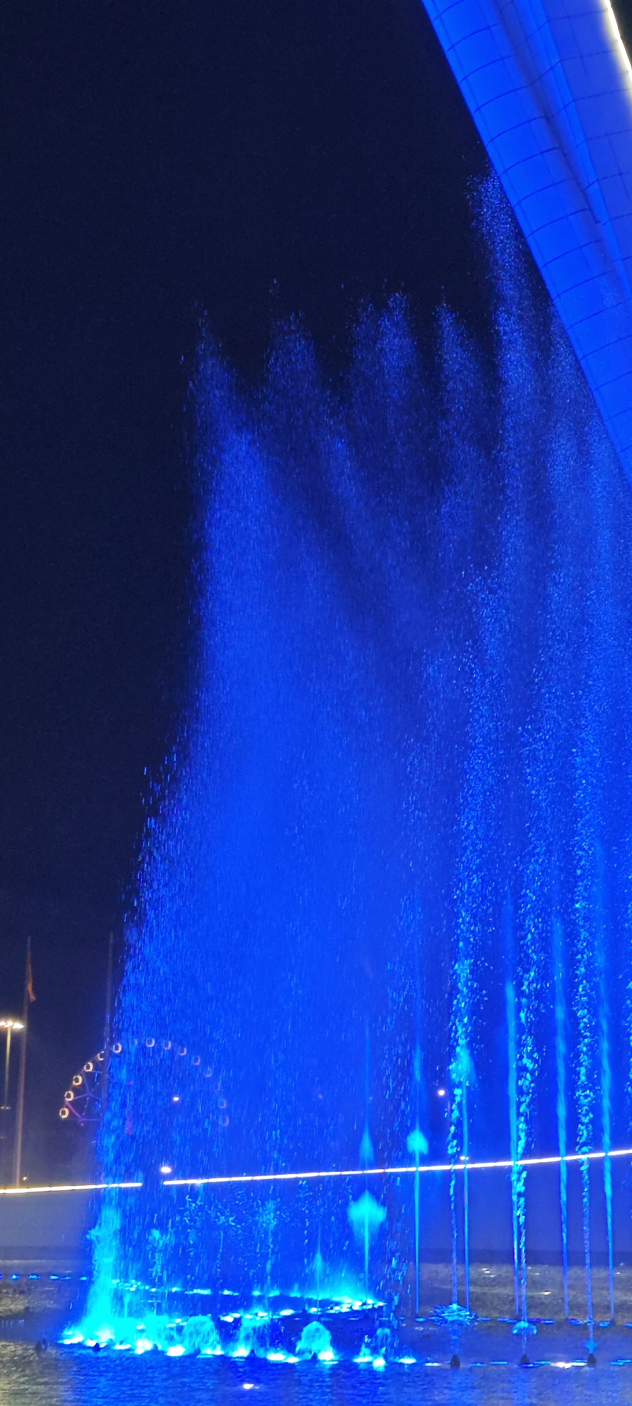 Blue fountain display observed with distant Ferris wheel visible