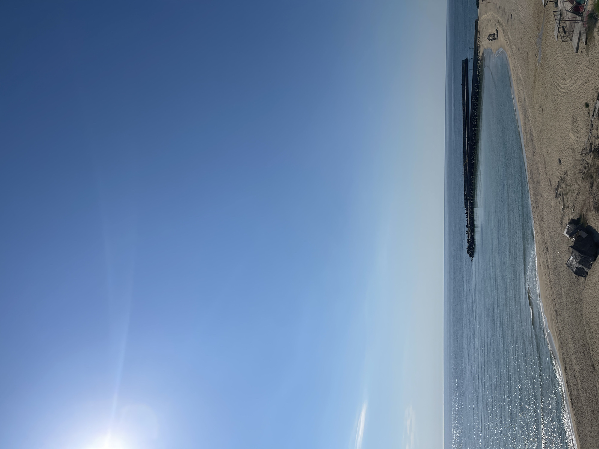 Aerial beach view shows pier, calm waters on sunny morning