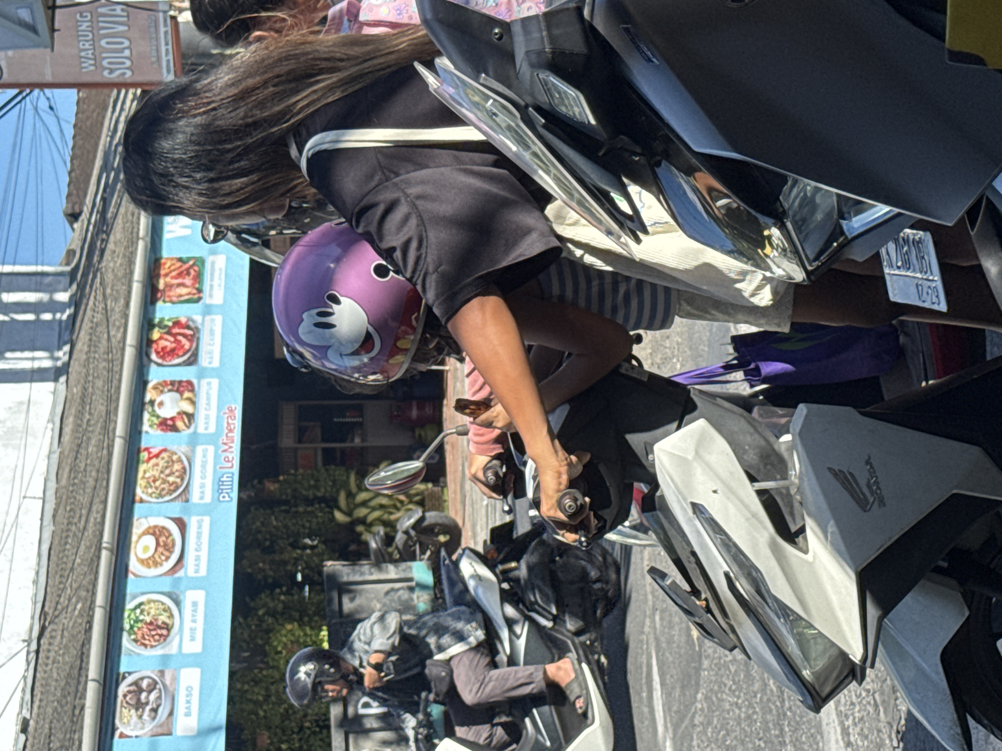 Morning scooter traffic flows past a roadside deity statue in Kuta Selatan