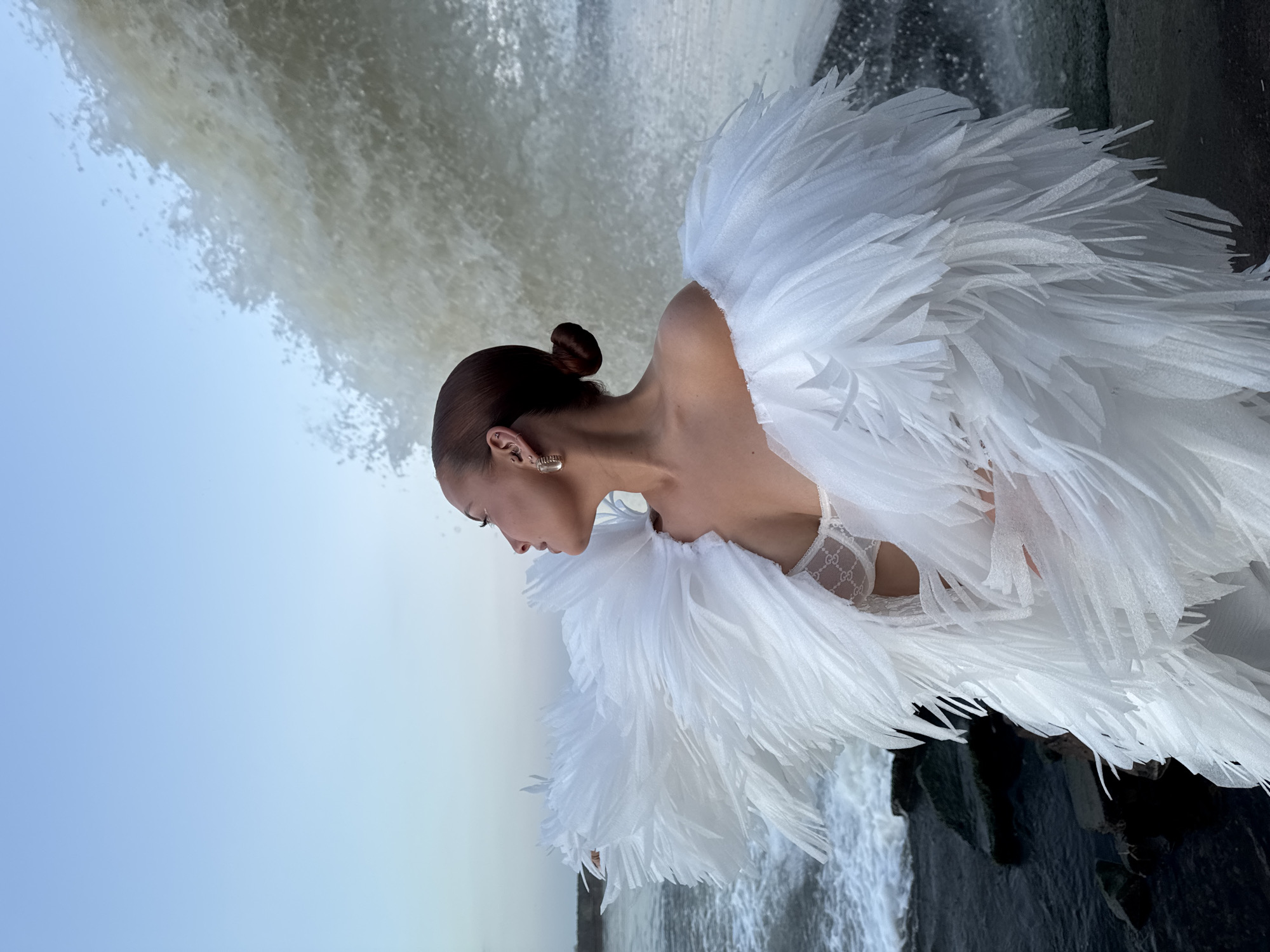 Woman in feathered dress poses by waterfall in Chaikovsky