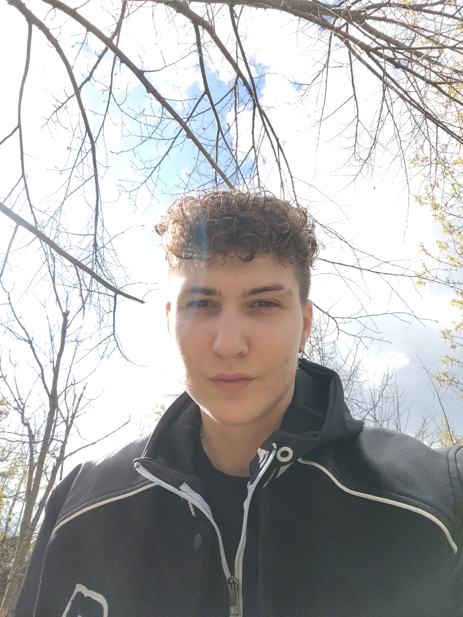 Person takes outdoor selfie under bare trees, cloudy sky
