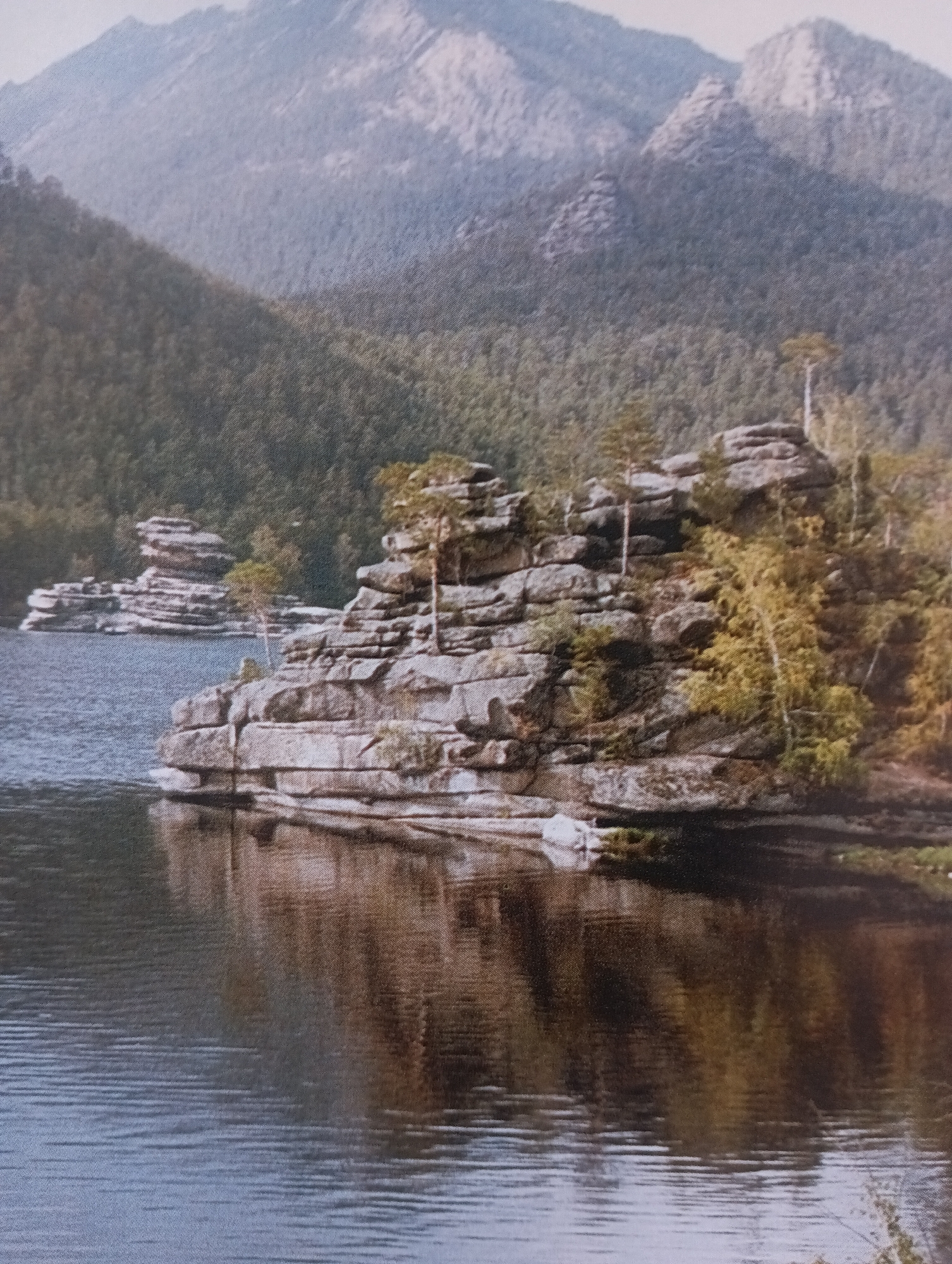 Still mountain lake with rocky outcrops and forested peaks