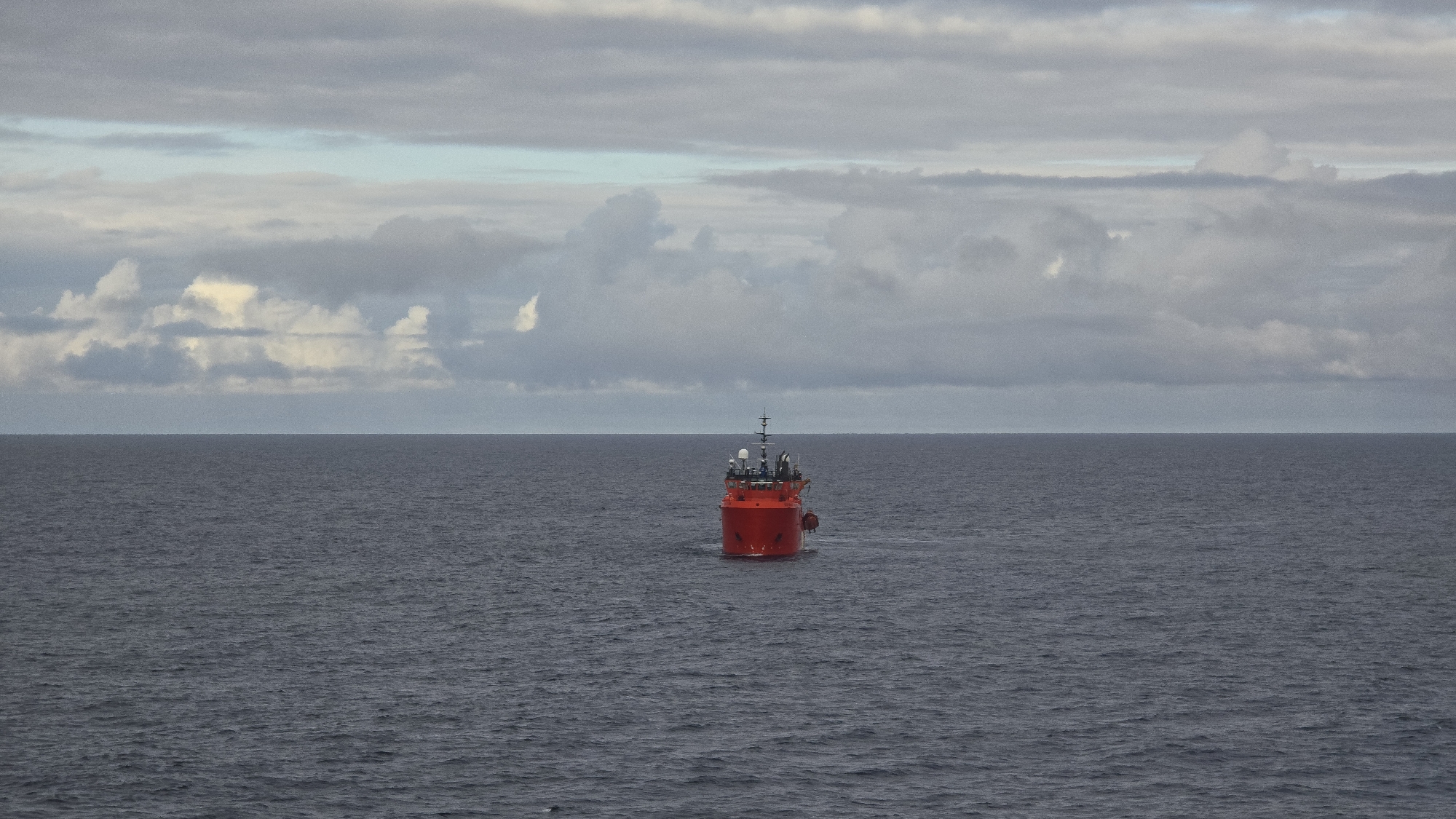 Red ship spotted on calm waters under grey skies