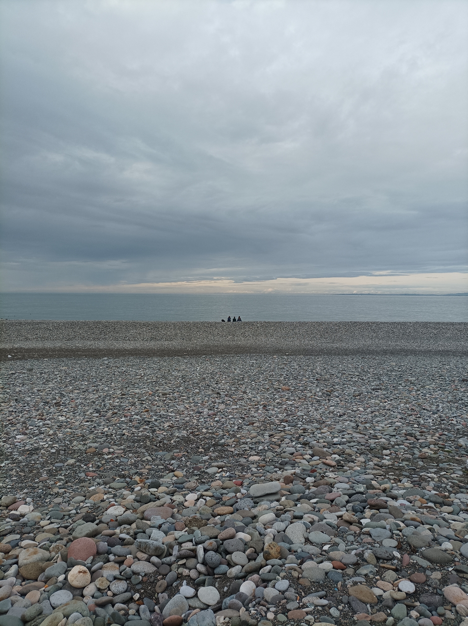Tourists gather at Batumi's pebble beach under cloudy skies