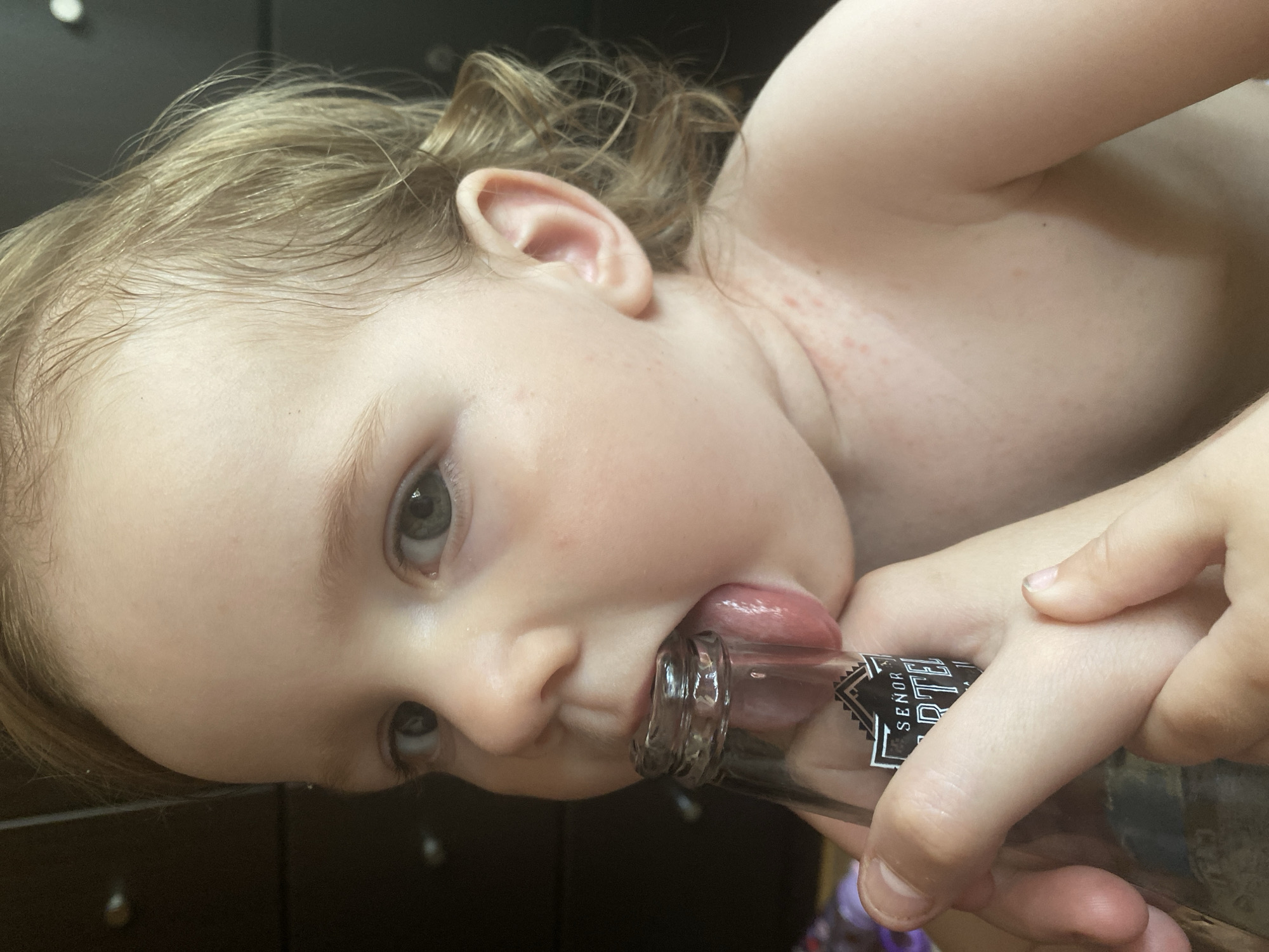 Toddler mouths beer bottle rim alongside Cartel beer close-ups