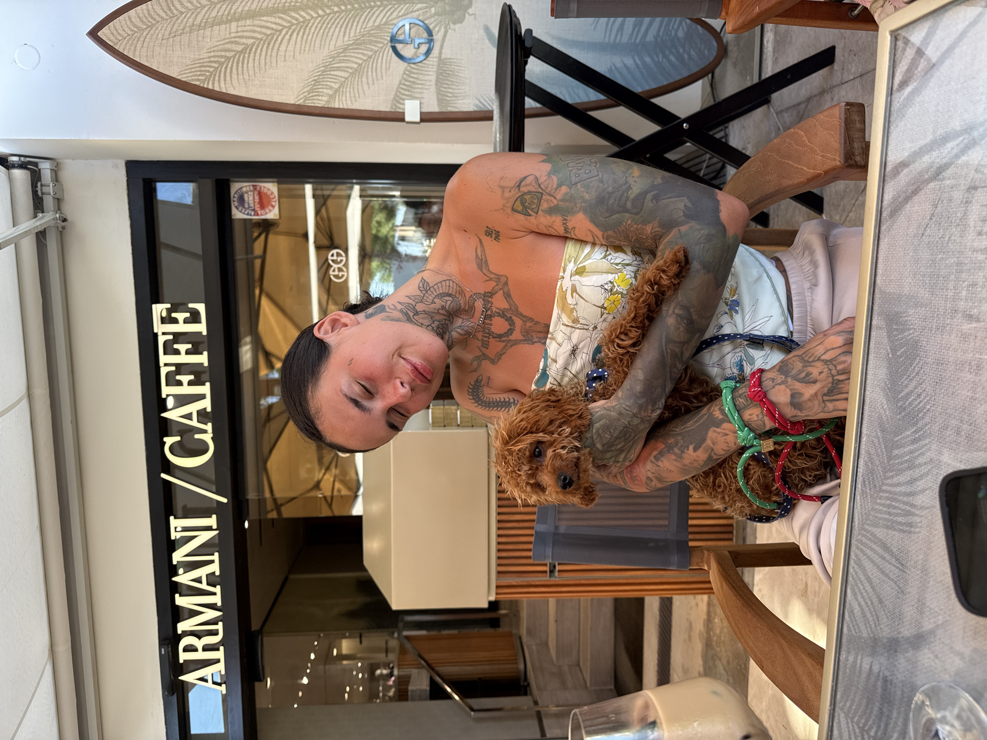 Tattooed arms cradling a curly dog with a colorful rope collar