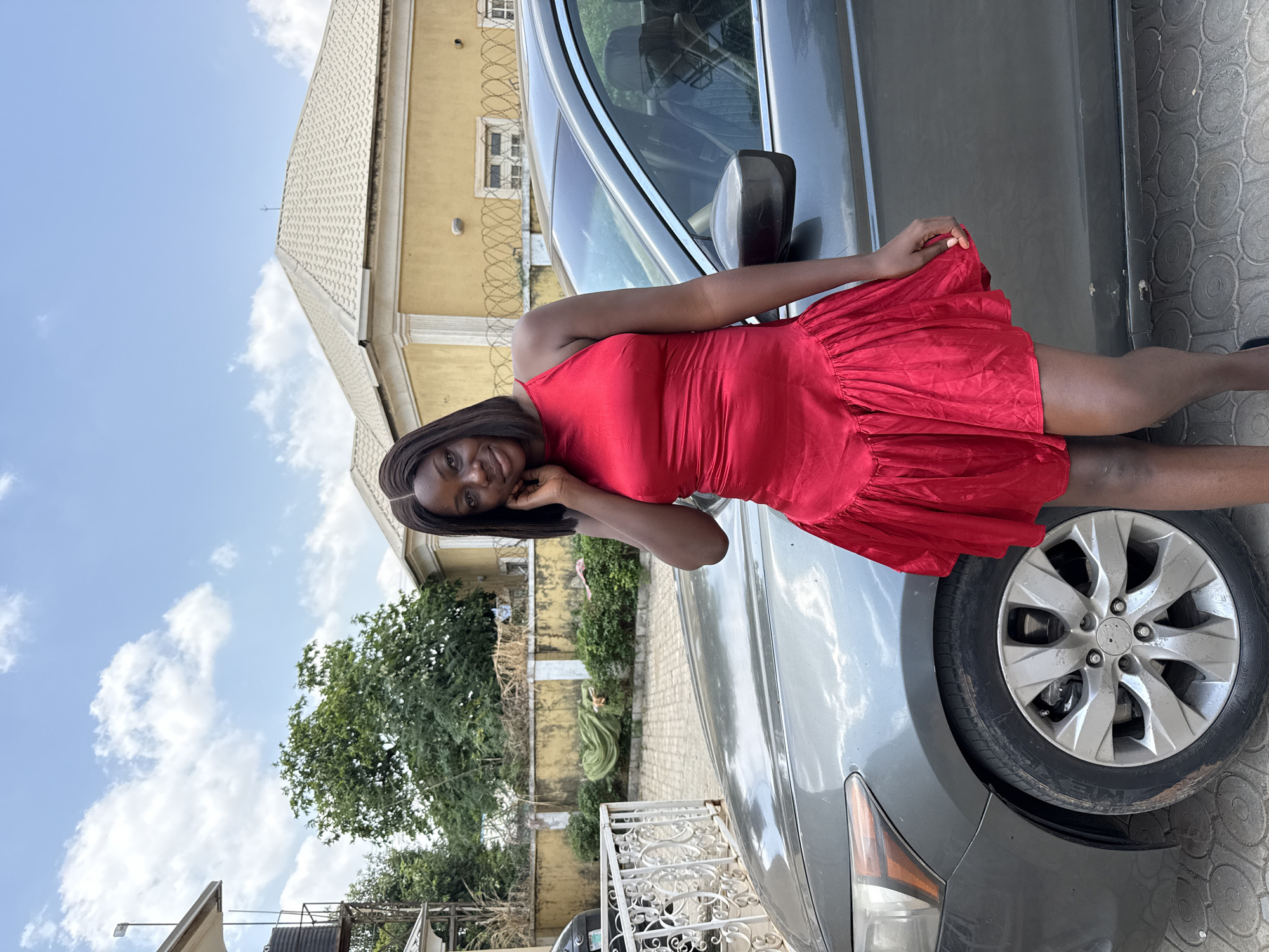 Woman poses in red dress beside car in Abuja