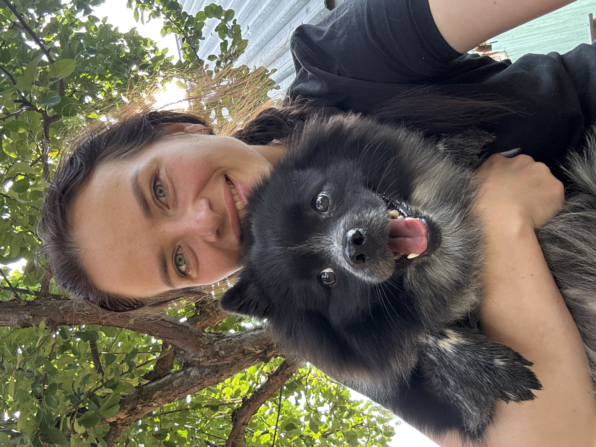 Fluffy dog and its person, all smiles outside a brick house