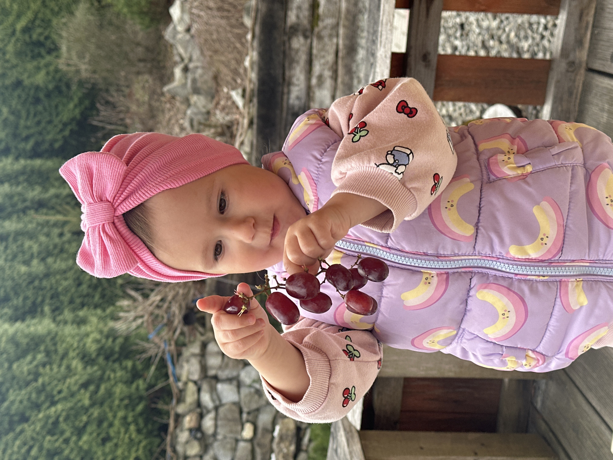 Baby in colorful winter outfit holds grapes in Wisła