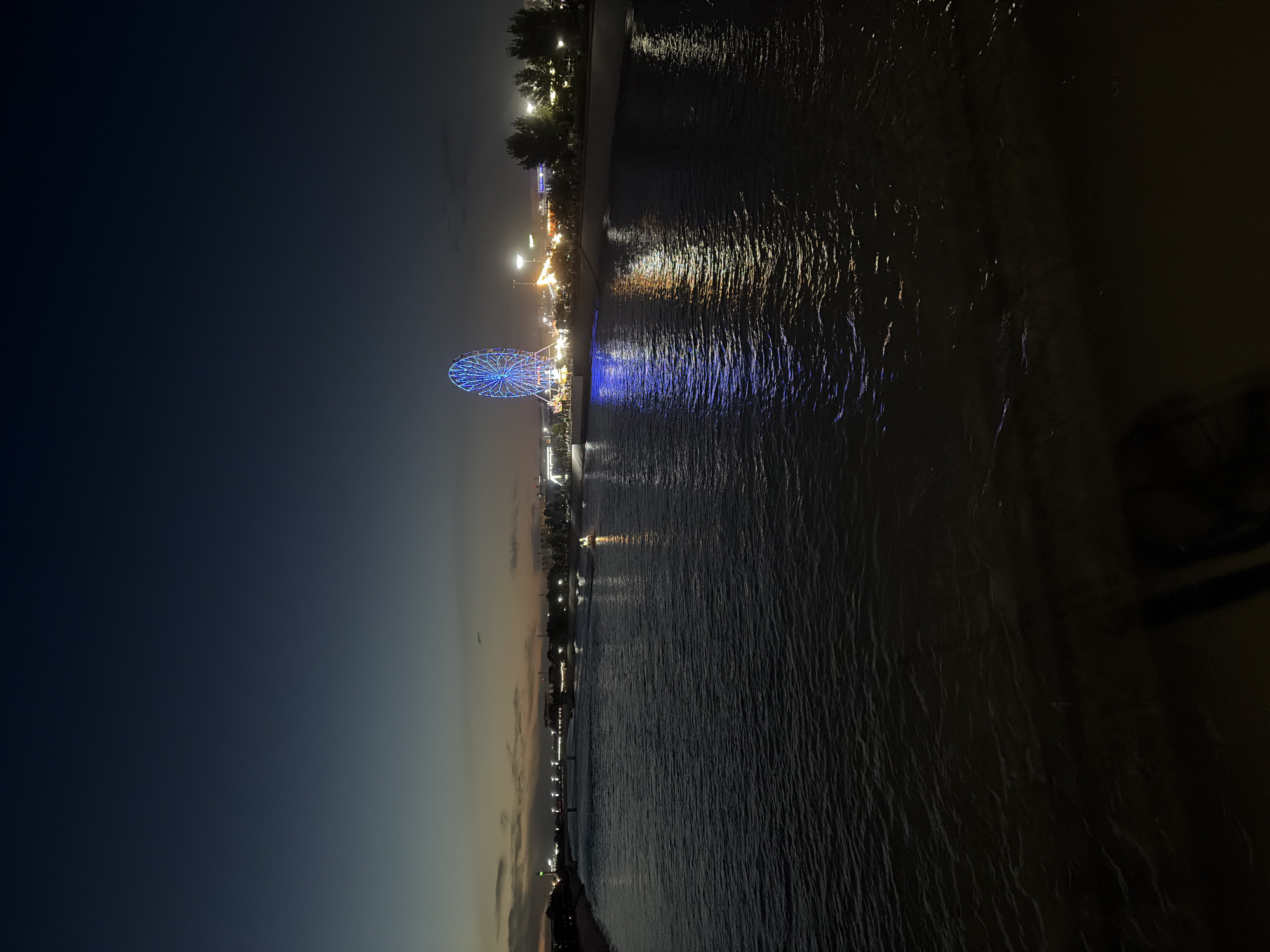 Blue-lit Ferris wheel glows on a Nukus waterfront pier at night