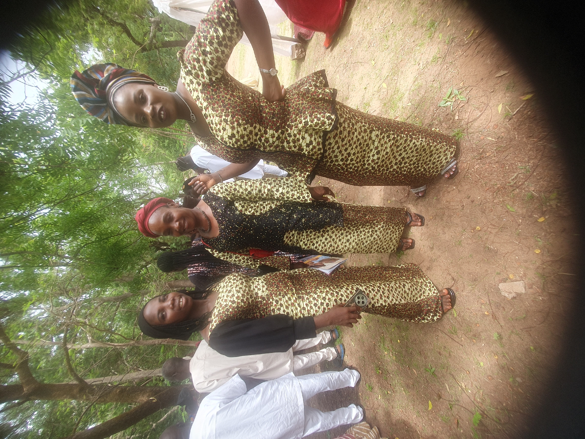 Three women in matching dresses gather in grassy area