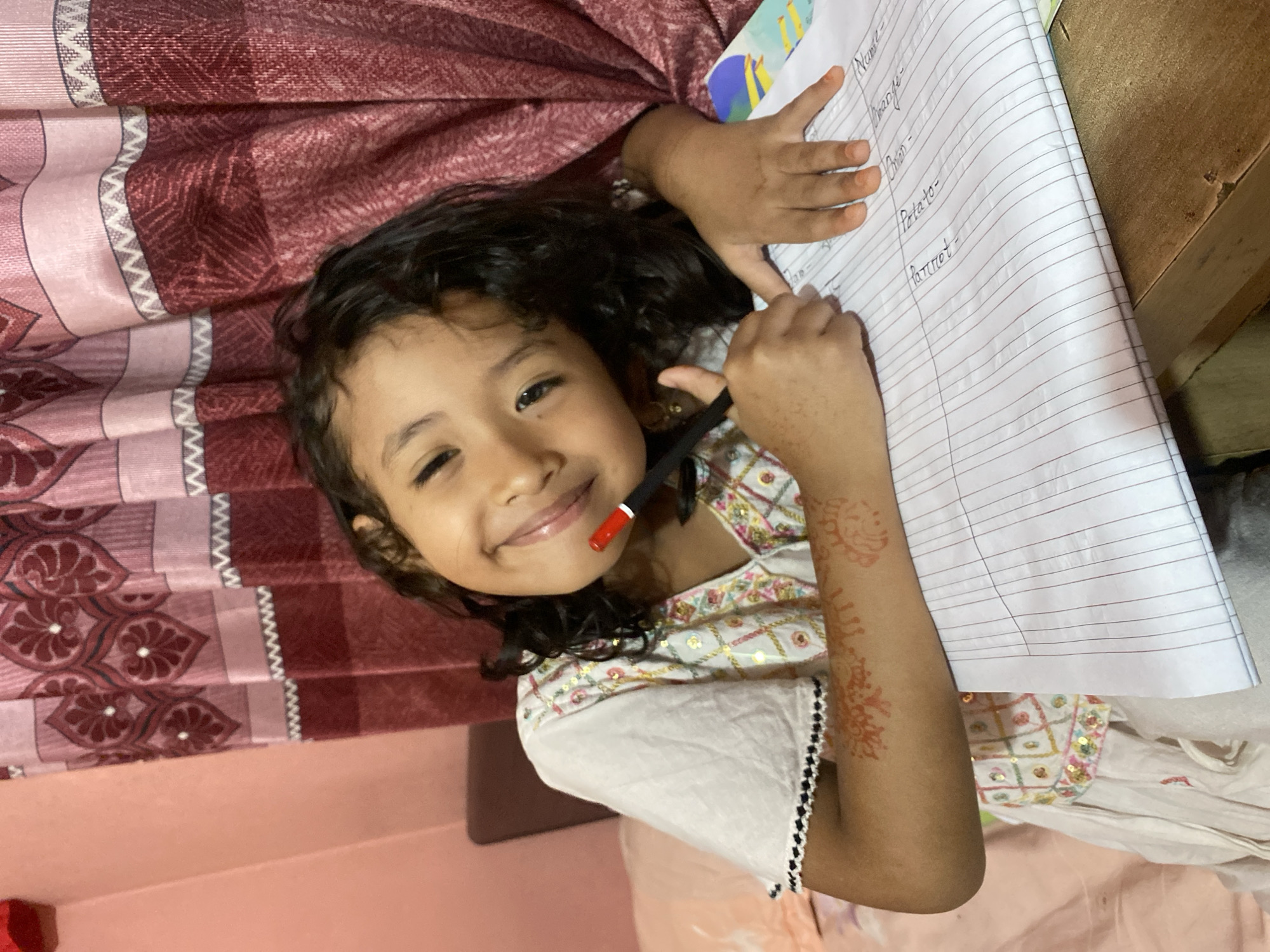 Writing in a notebook in Dhaka, henna-adorned arm on the page