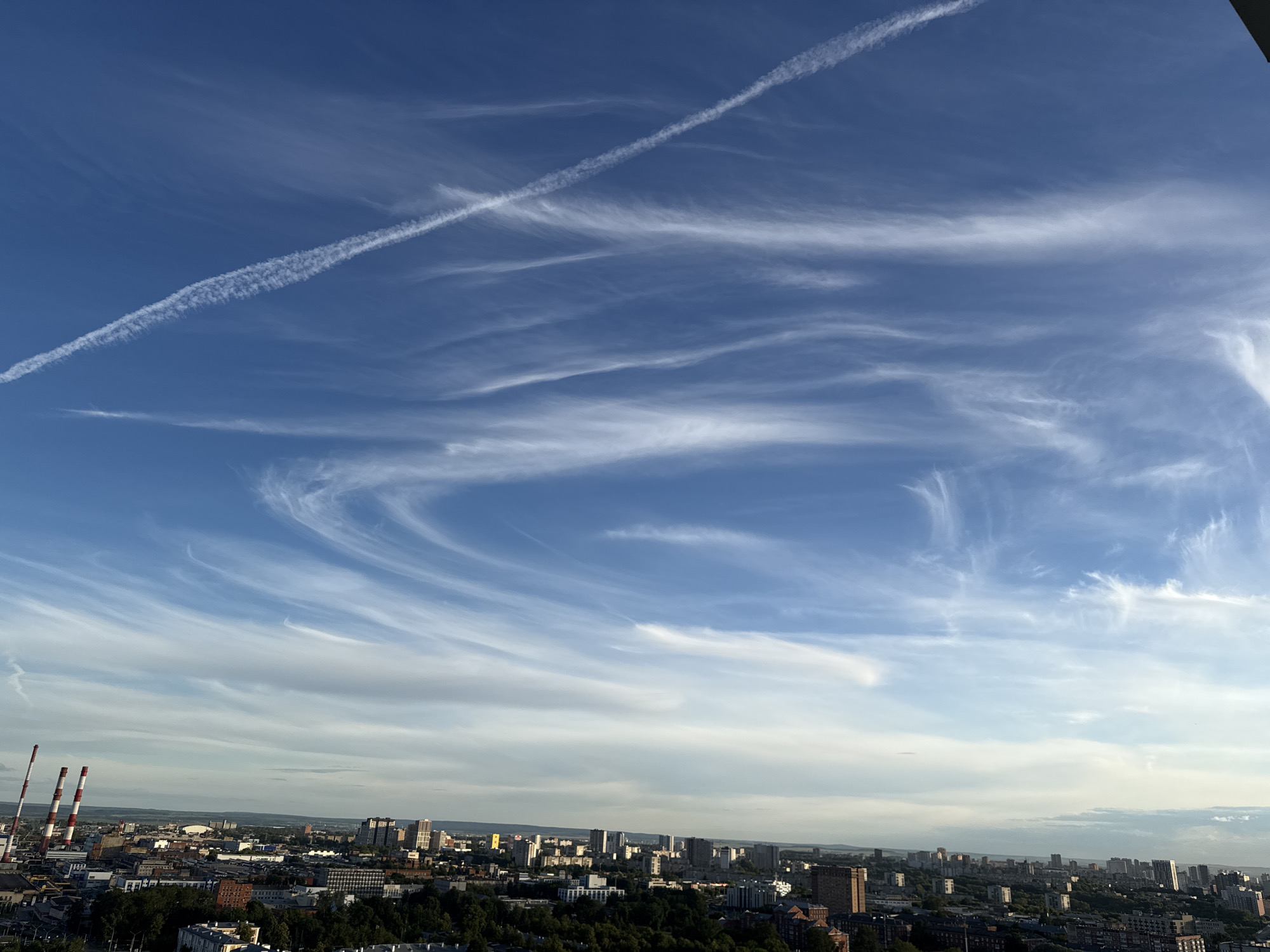 City skyline under open blue skies with contrails overhead
