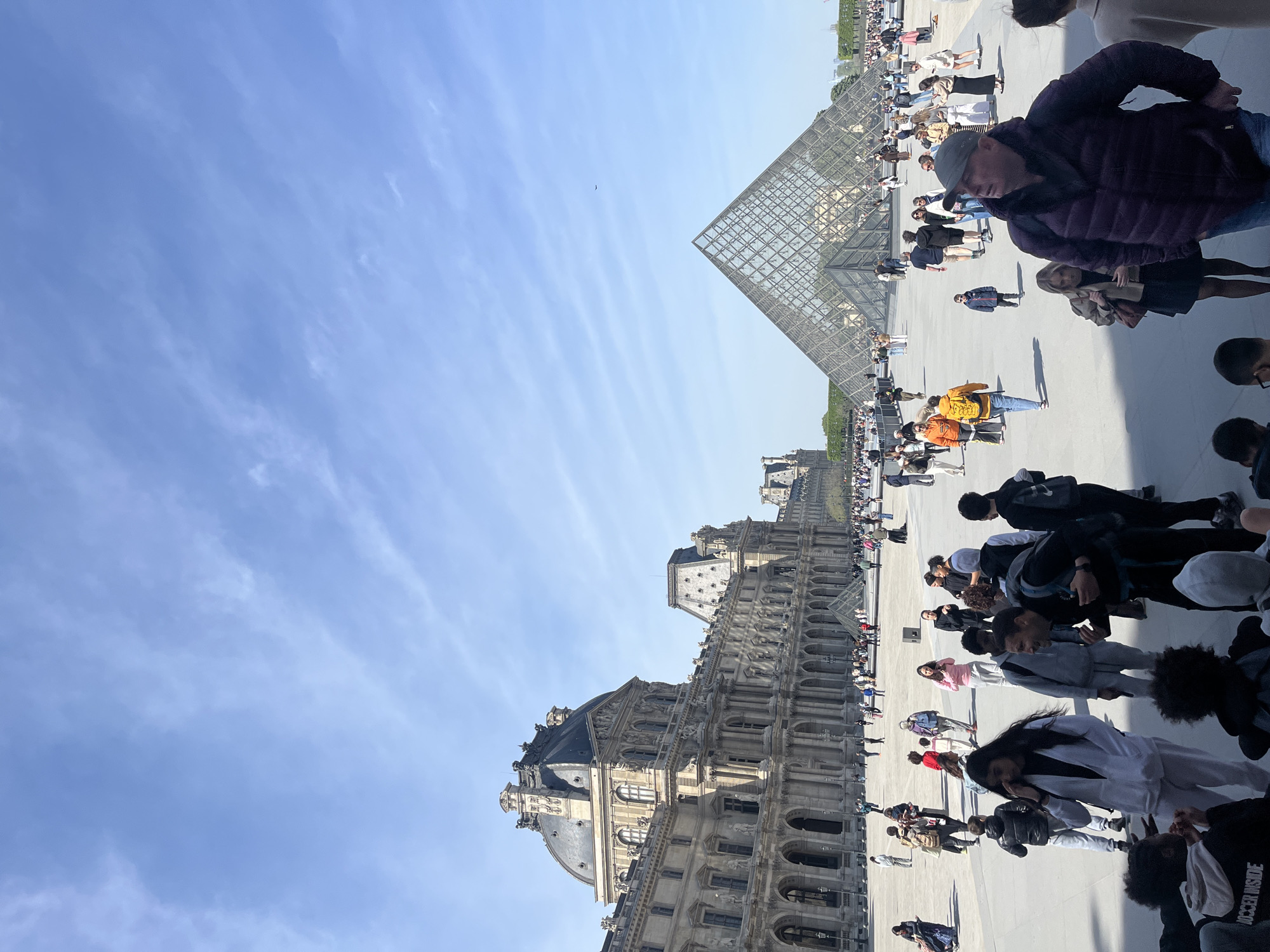 Crowds gather at Louvre Museum plaza under clear skies