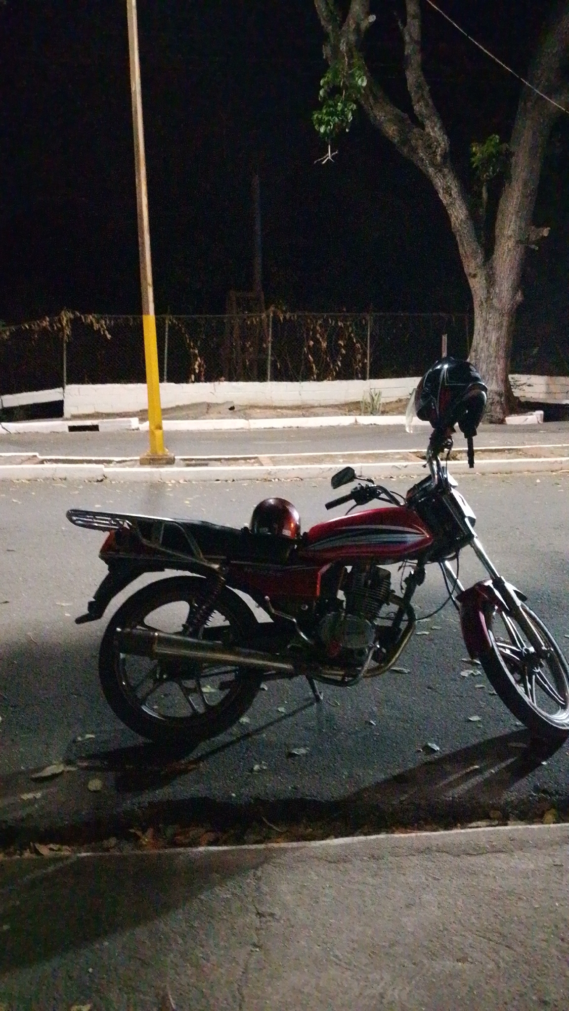 Red motorcycle with helmet parked on Tinaquillo street at night
