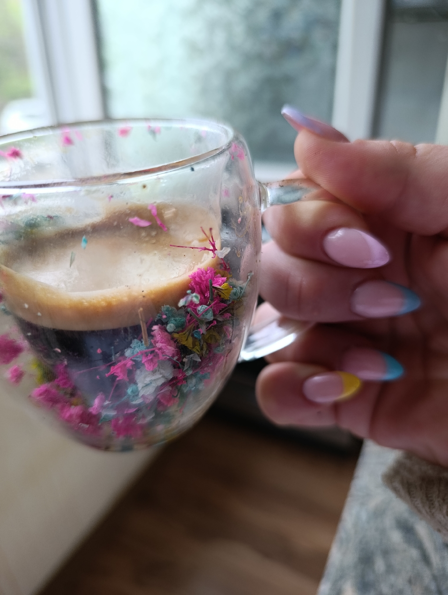 Person displays colorful manicure while holding floral glass mug