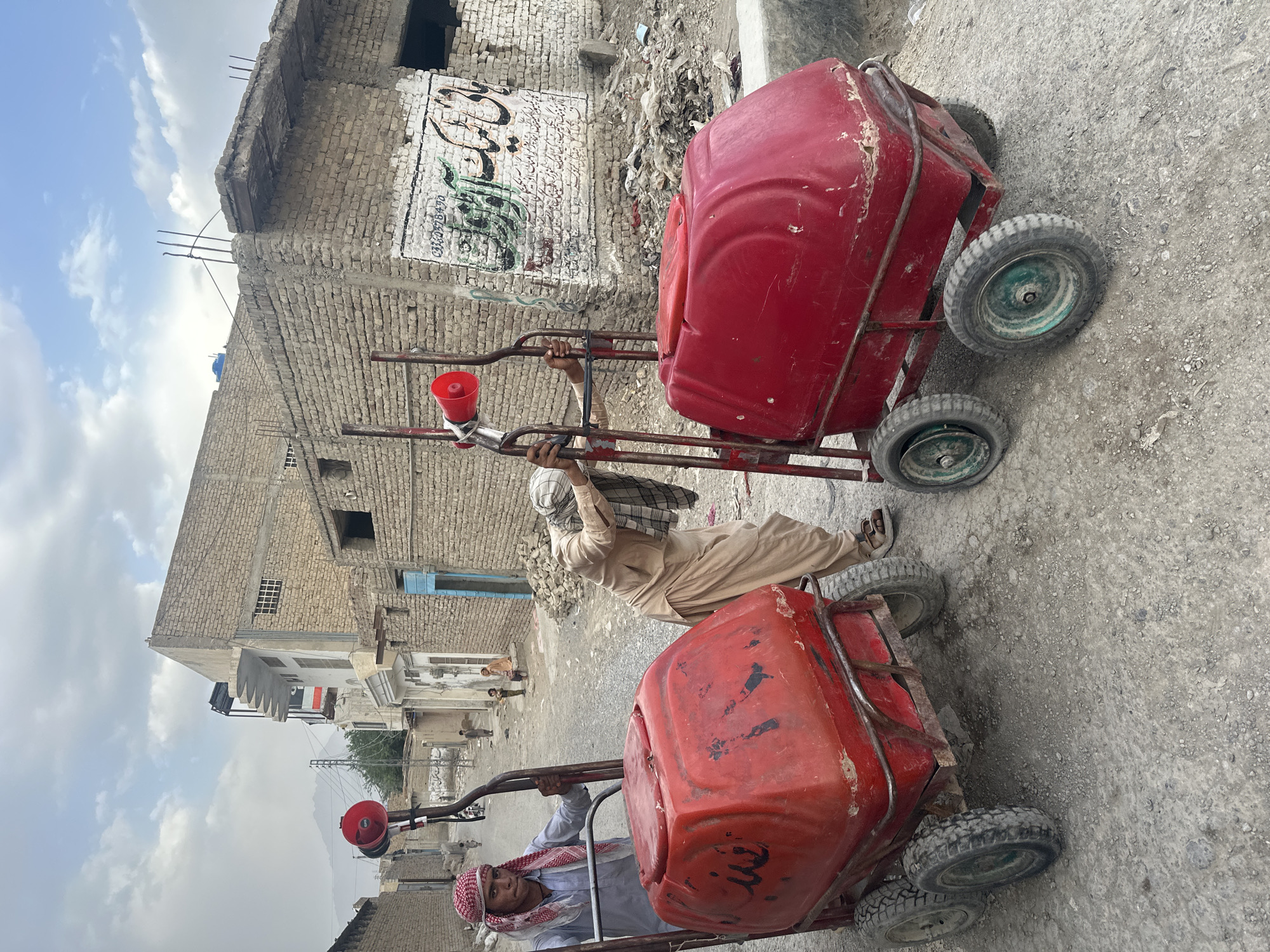 Two people pull red carts on unpaved Quetta street
