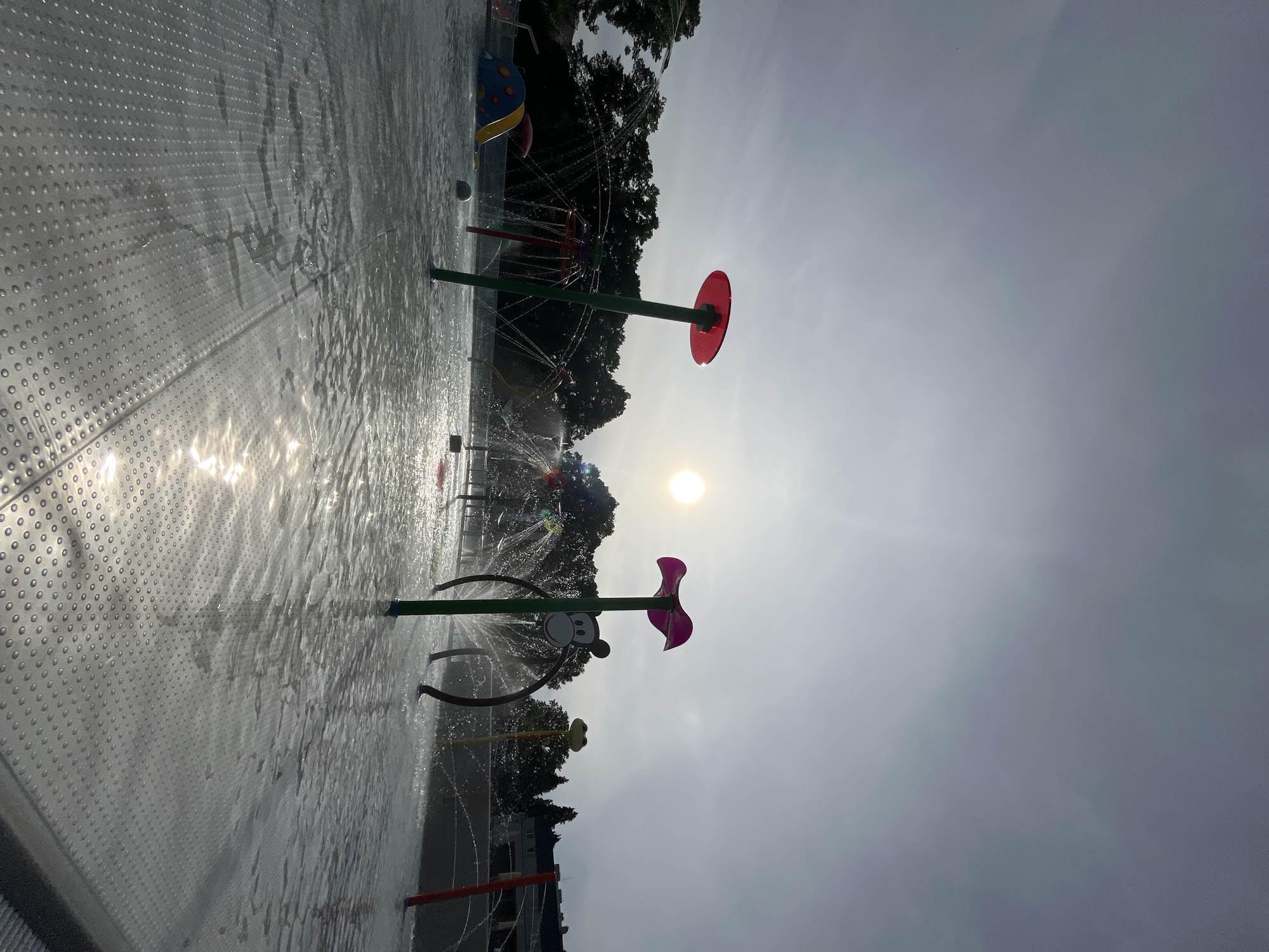Outdoor pool and splash pad facility documented under varied sky