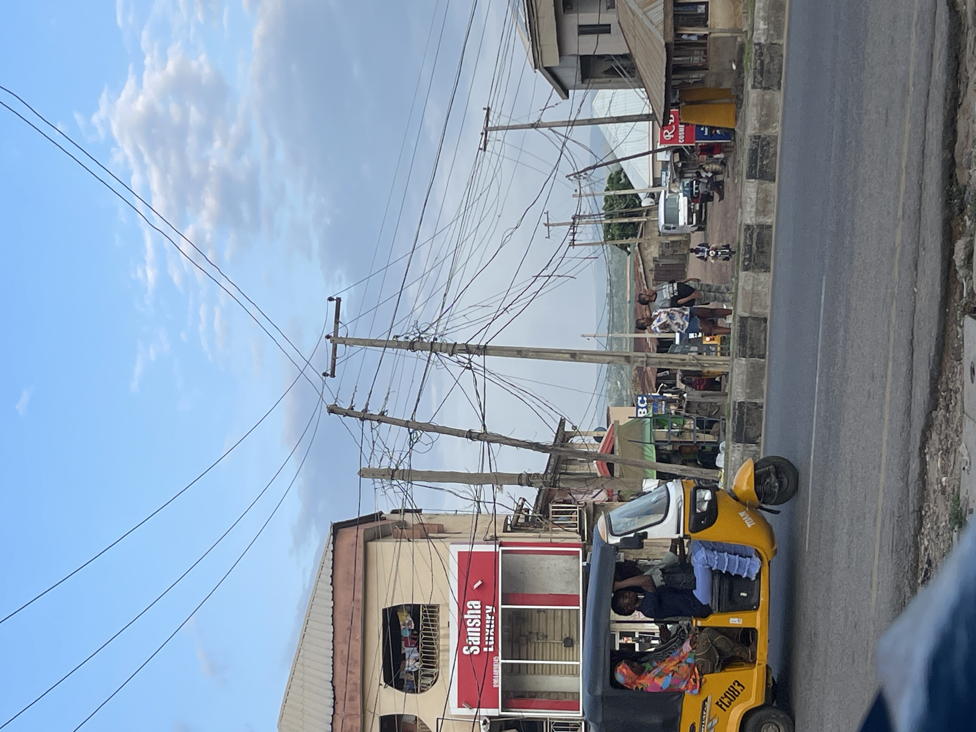 Nigerian city street buzzing with keke napeps, motos, and foot traffic
