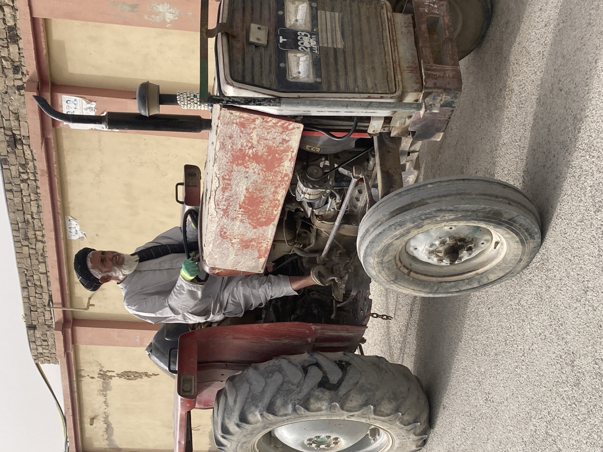 Elderly farmer repairs tractor engine in Quetta, Pakistan