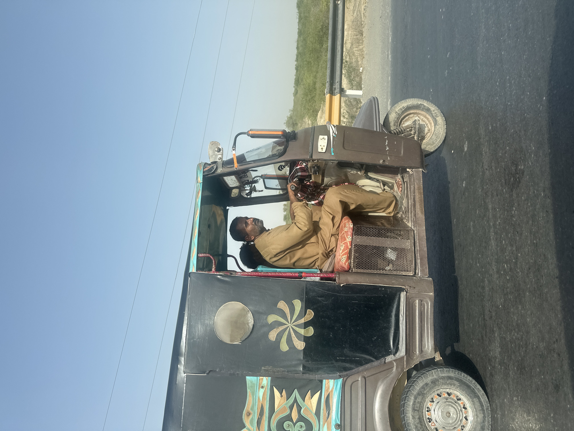 Decorated auto-rickshaw rolling down a sunny Pakistani road