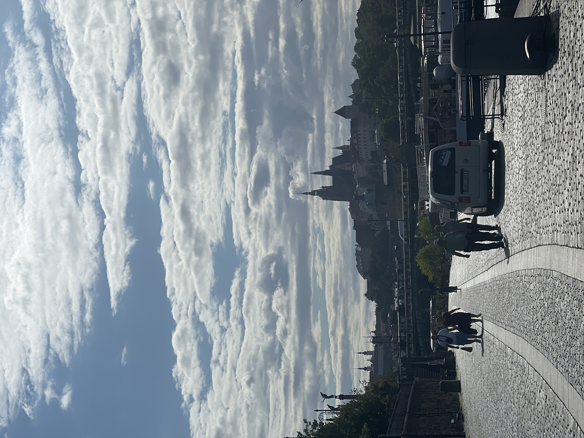 Strolling a cobblestone riverside path with city spires ahead