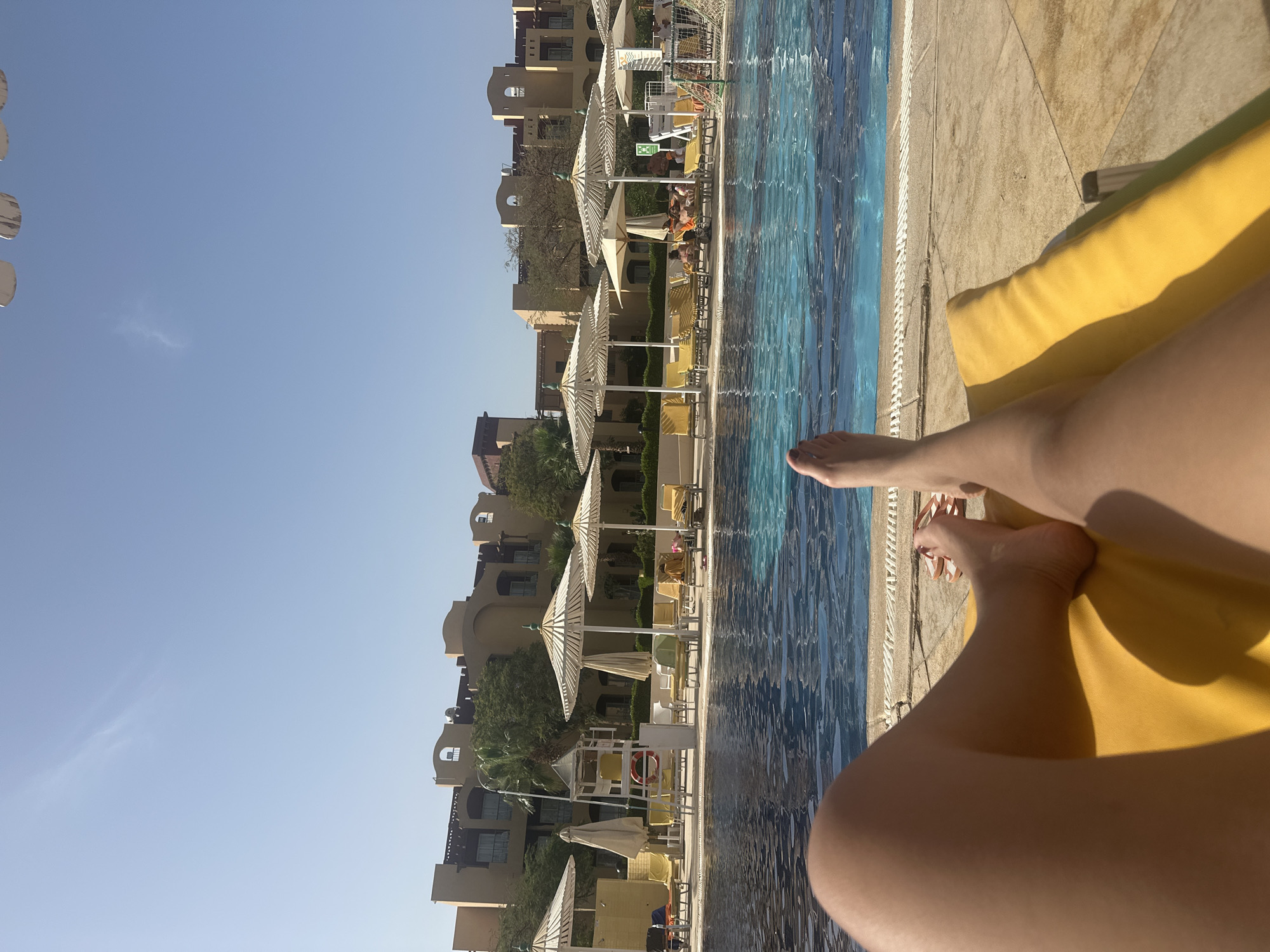 Person relaxes on yellow lounge chair by resort pool